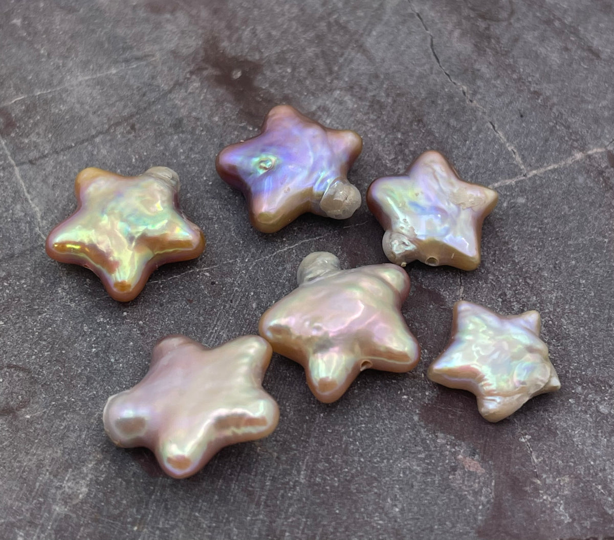 Five iridescent star-shaped baroque pearls arranged on a dark gray textured stone surface.