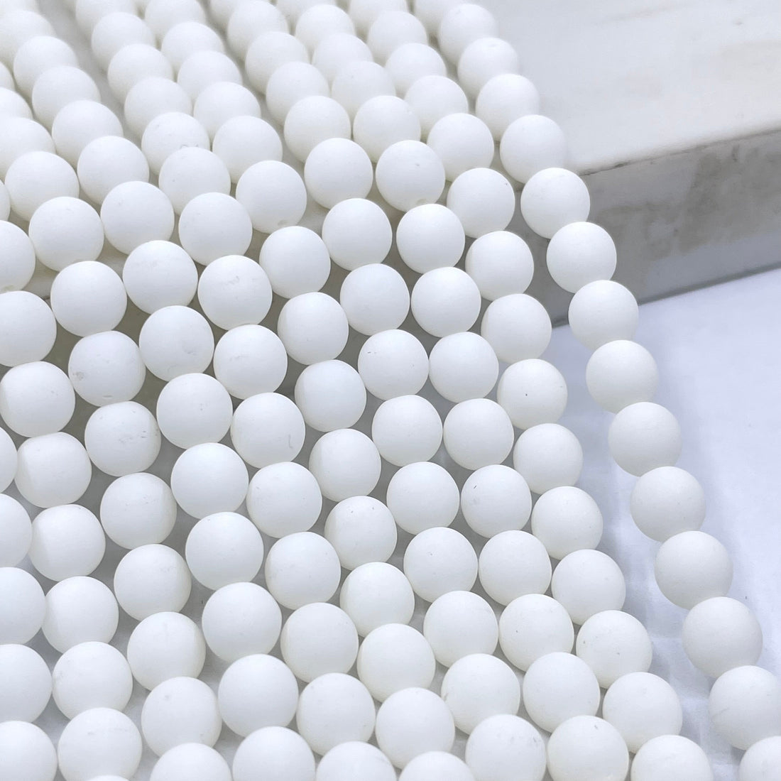 Velvet White round glass beads arranged in parallel strands on a light marble surface.