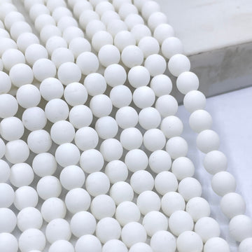 Velvet White round glass beads arranged in parallel strands on a light marble surface.