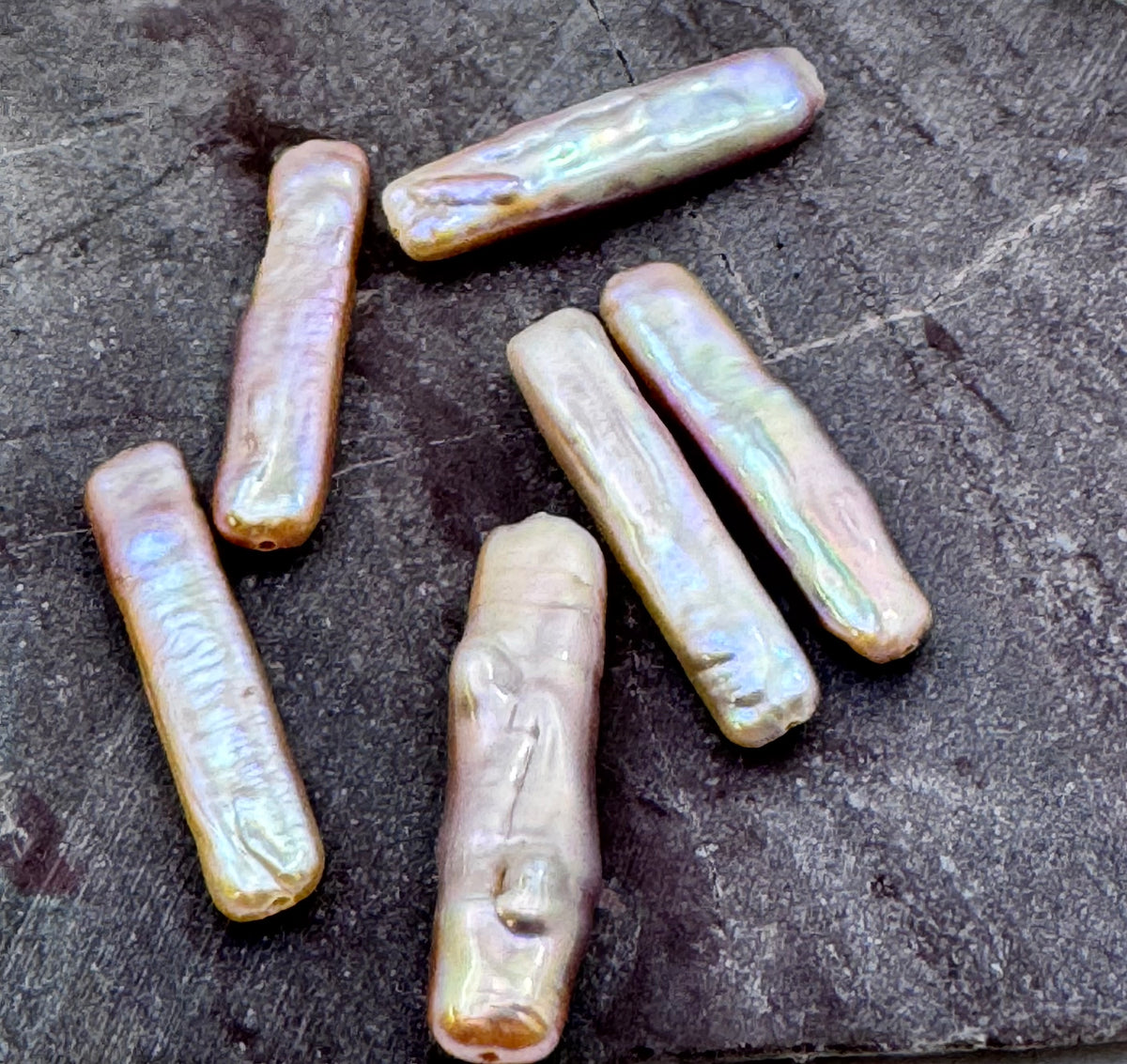 Six natural baroque pearl beads with an iridescent finish, displayed on a dark textured slate surface.