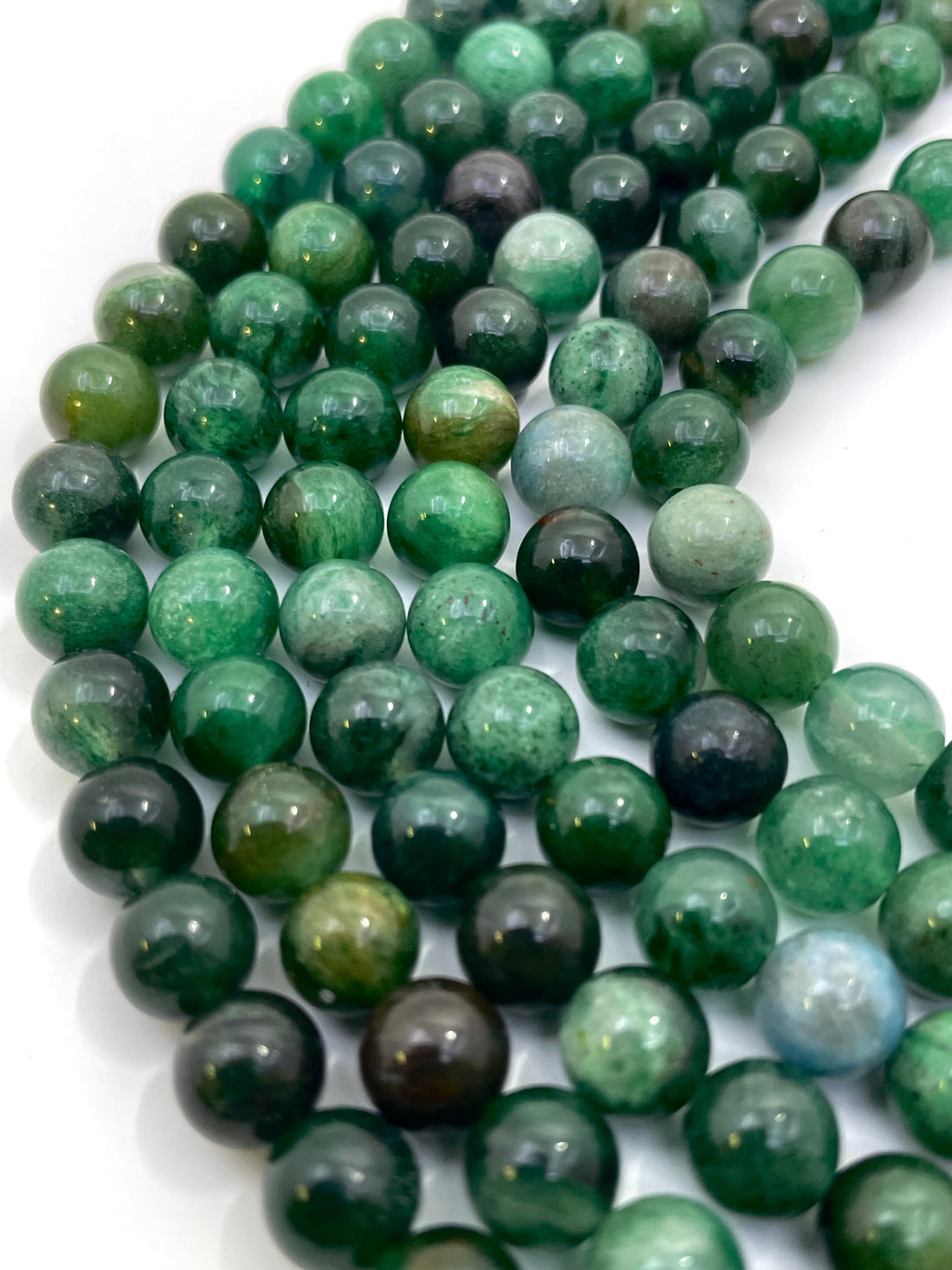 Multiple strands of polished round green lepidolite gemstone beads, varying from light forest green to dark emerald with natural inclusions, arranged on a plain white background.