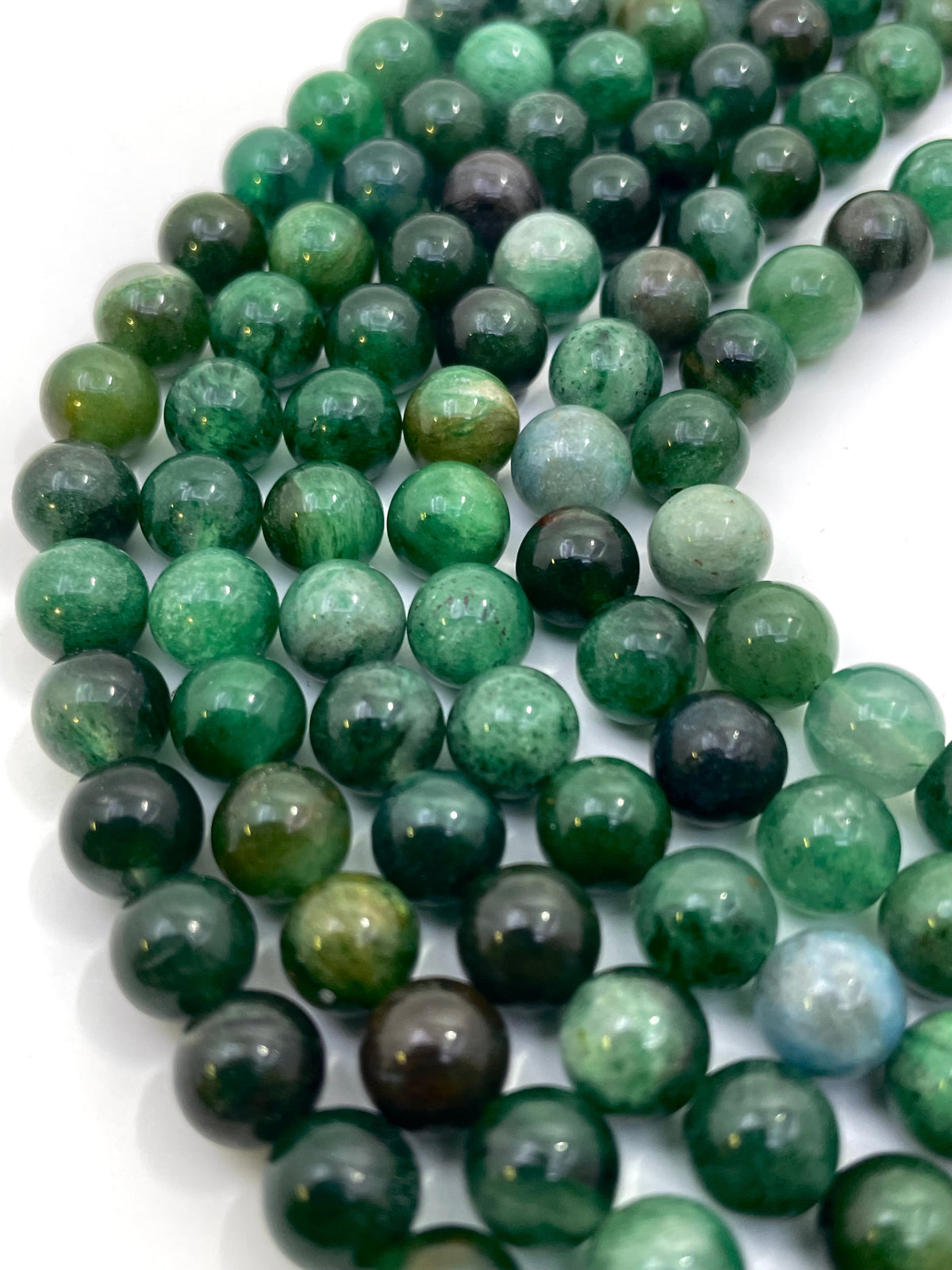 A close-up of glossy round green lepidolite gemstone beads arranged in curved strands on a white background.