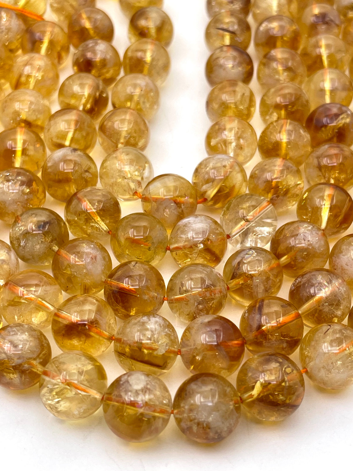 Close-up of a strand of round citrine beads in a translucent golden yellow color with natural inclusions, strung on a cord against a white background.