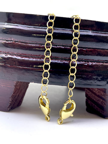 Two gold lobster claw chain extender links with spring rings, displayed on a dark wooden block against a white background.