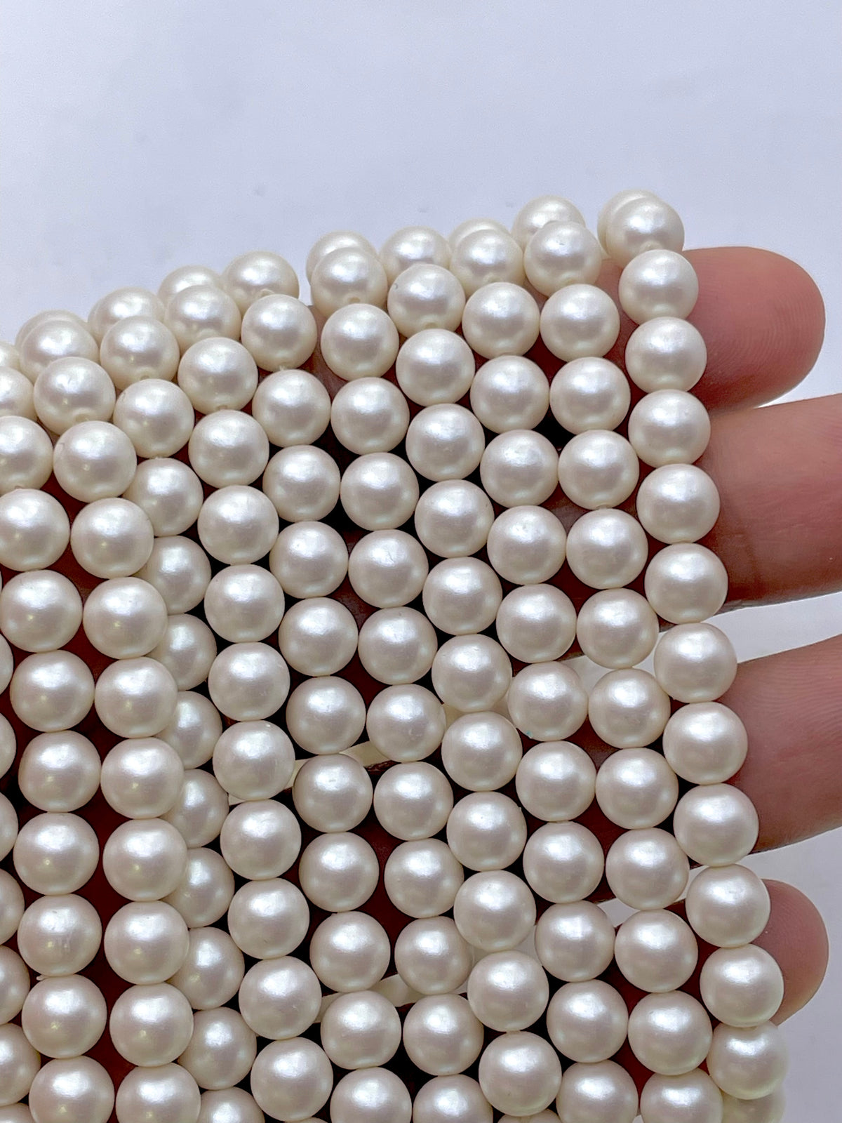 Pearlescent ivory shell pearls shown on a hand for size reference