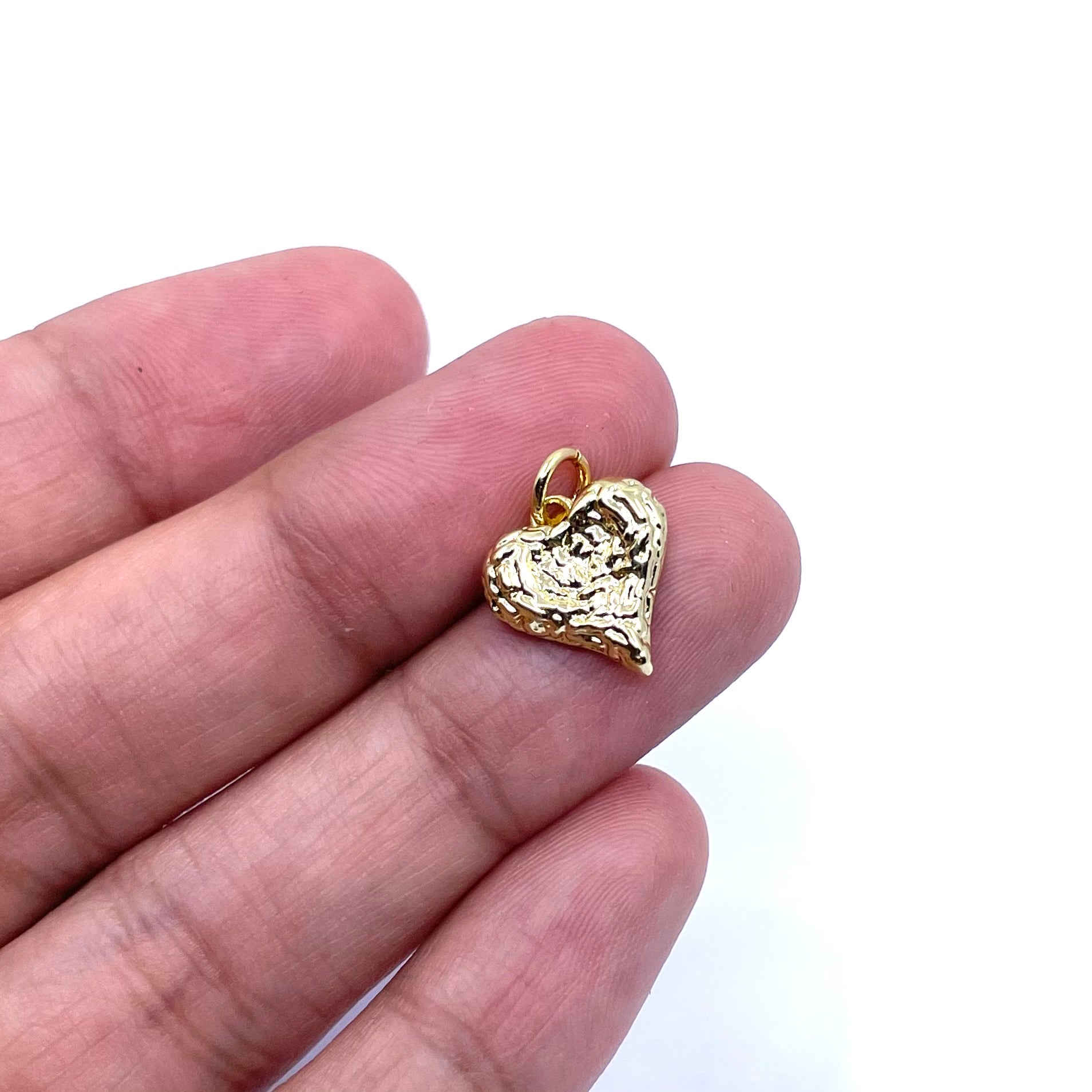 A small textured gold heart-shaped pendant held on a person's fingers against a plain white background.
