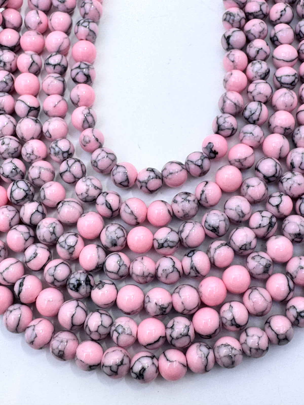 Multiple strands of round pink howlite beads with black and gray marbled patterns, arranged in a U-shape on a plain white background.
