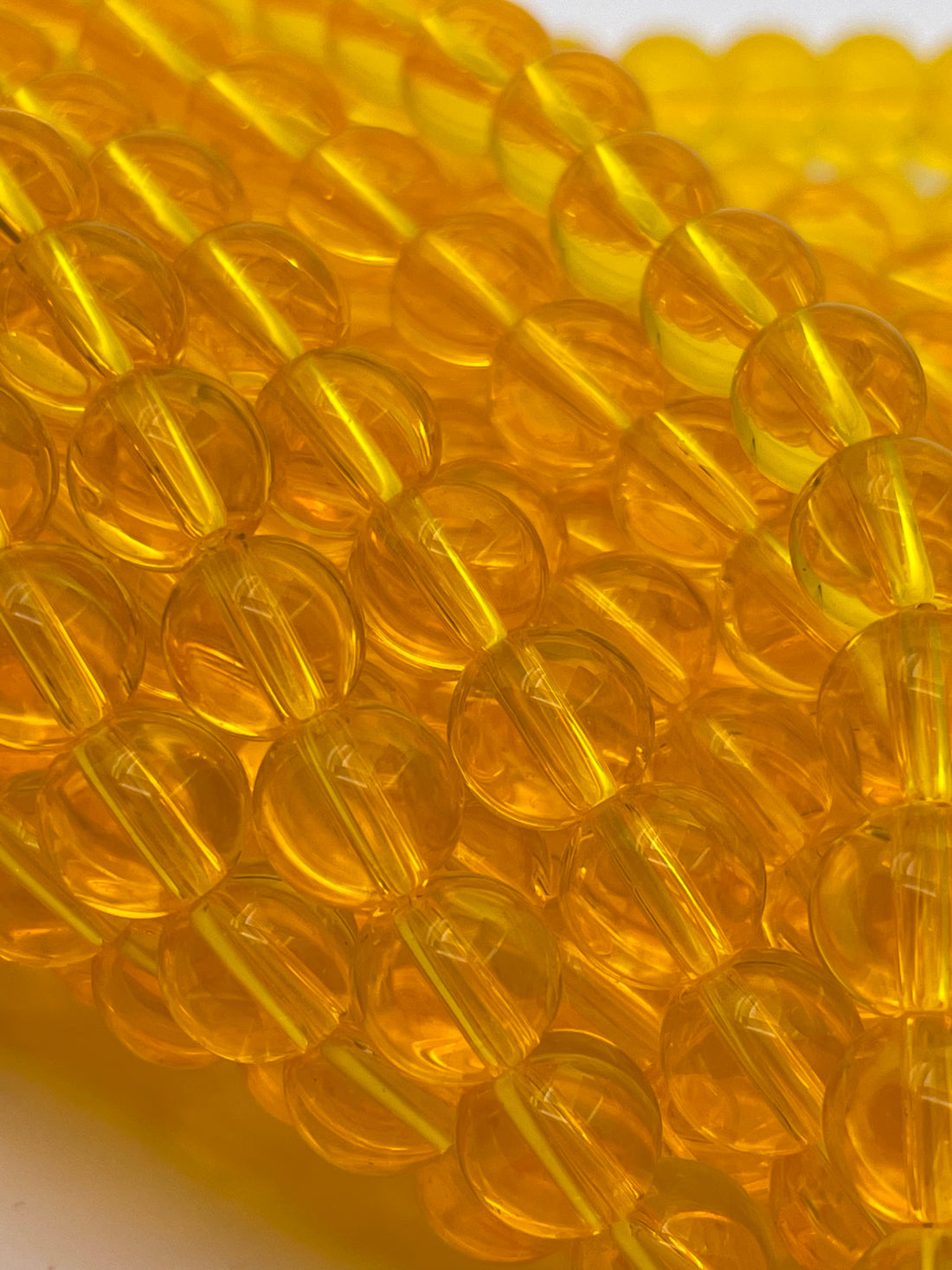 A close-up of translucent amber yellow glass beads strung together on a white background.