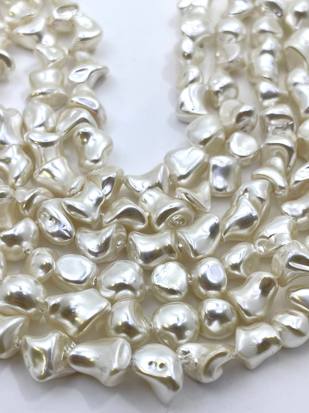 A close-up of a strand of irregular, glossy white shell pearl beads arranged in a curve on a plain white background.