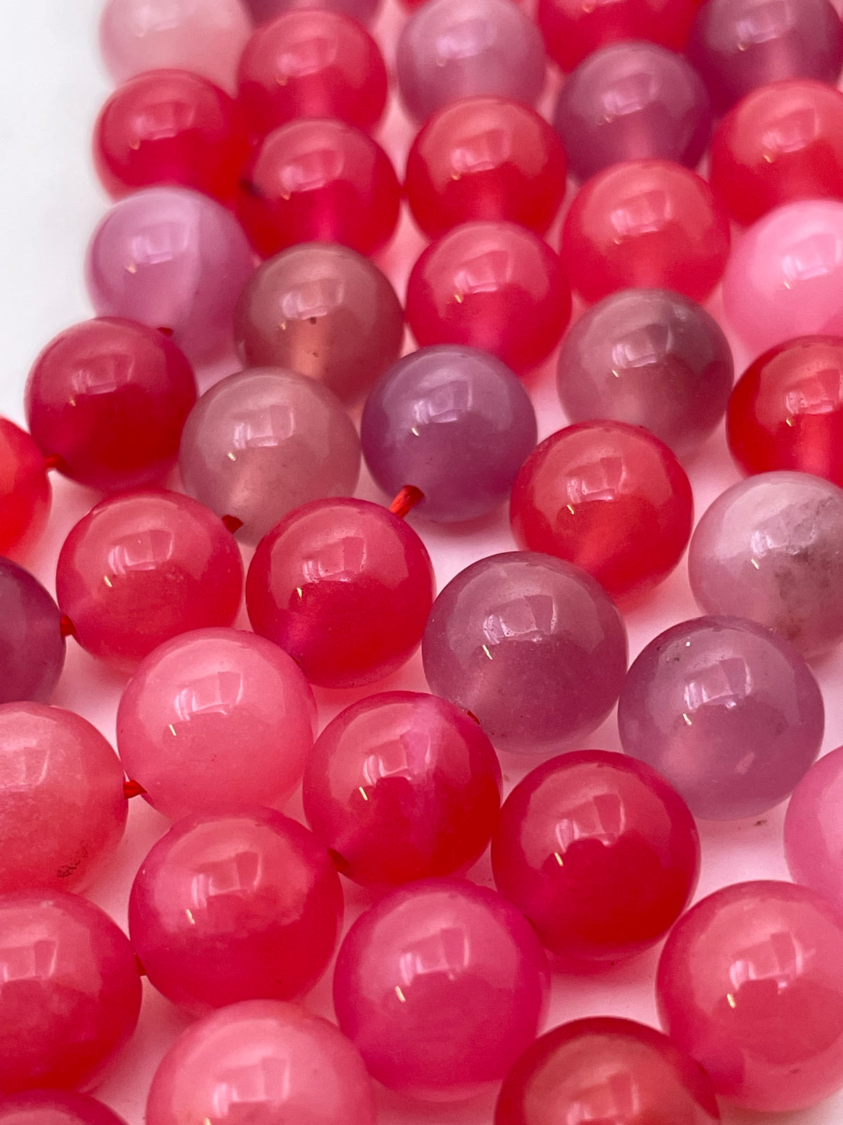 A close-up of glossy round scarlet agate beads in shades of pink, magenta, and purple, arranged tightly together on a white background.