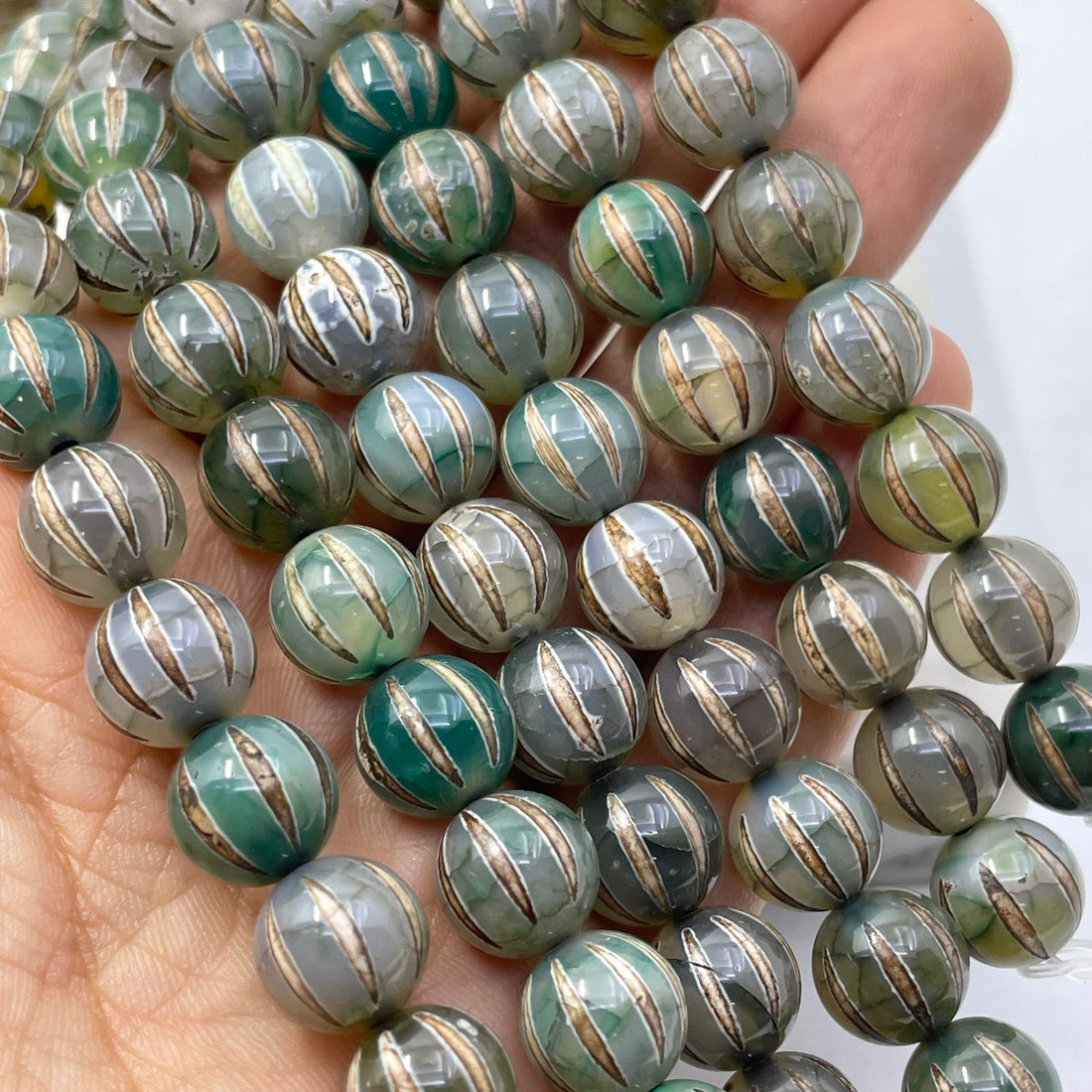 A close-up of round tibetan agate dzi beads strung in rows, featuring a marbled pattern of green, gray, white, and metallic gold vertical stripes.
