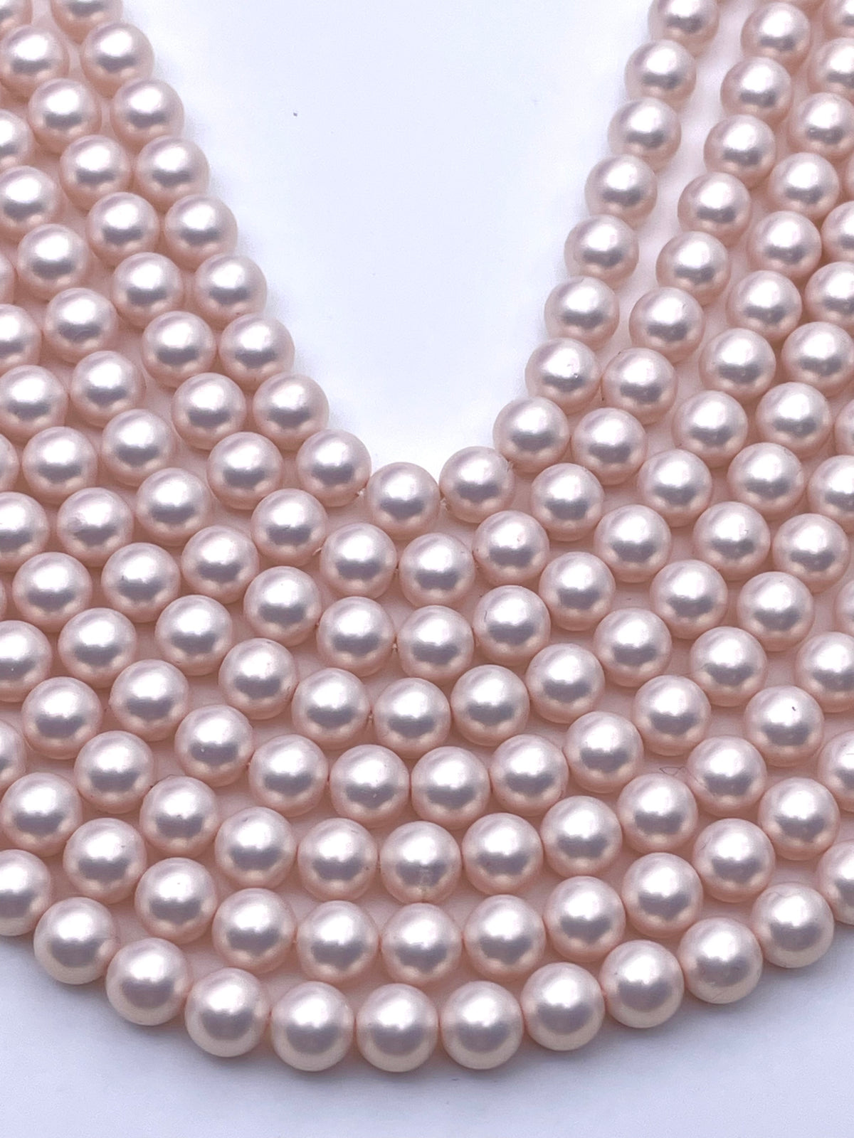 Multiple strands of light pink shell pearl beads arranged in a layered V-shape on a plain white background.