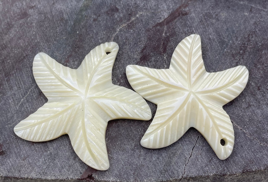 A hand holds a carved starfish-shaped pendant in the foreground, with two similar starfish pendants blurred in the background on a white surface.