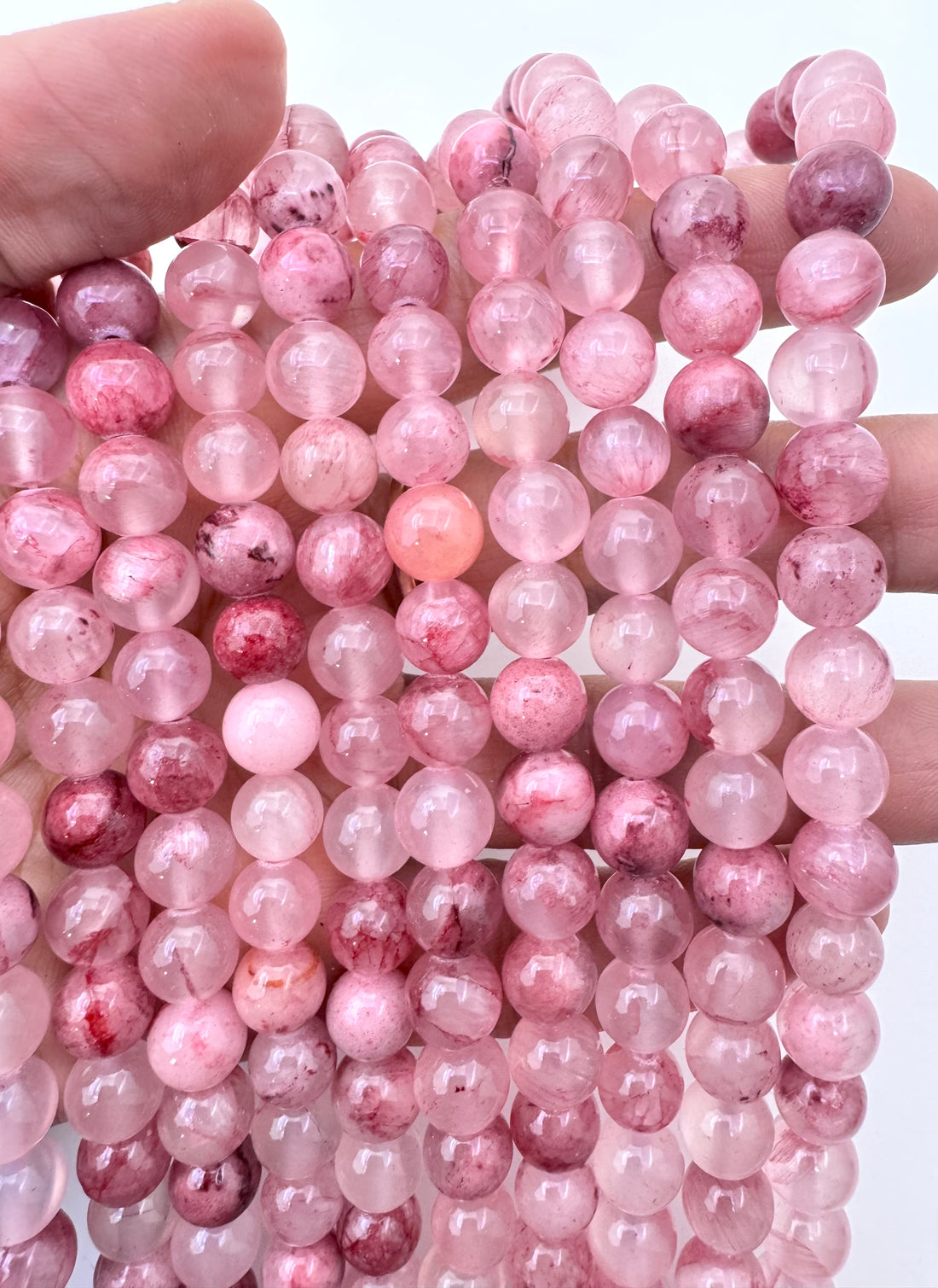 A close-up of multiple strands of round pink persian jade gemstone beads, arranged on a plain white background.