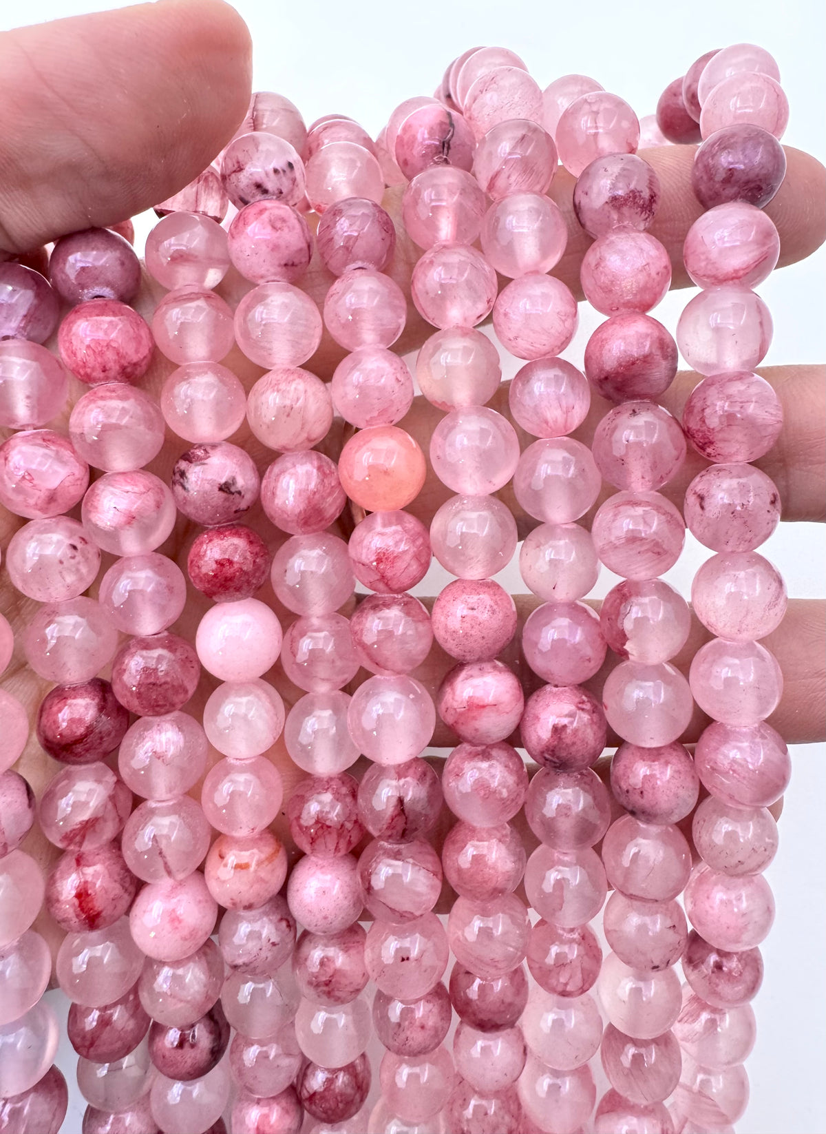 Multiple strands of round pink persian jade gemstone beads held in a hand against a plain white background.