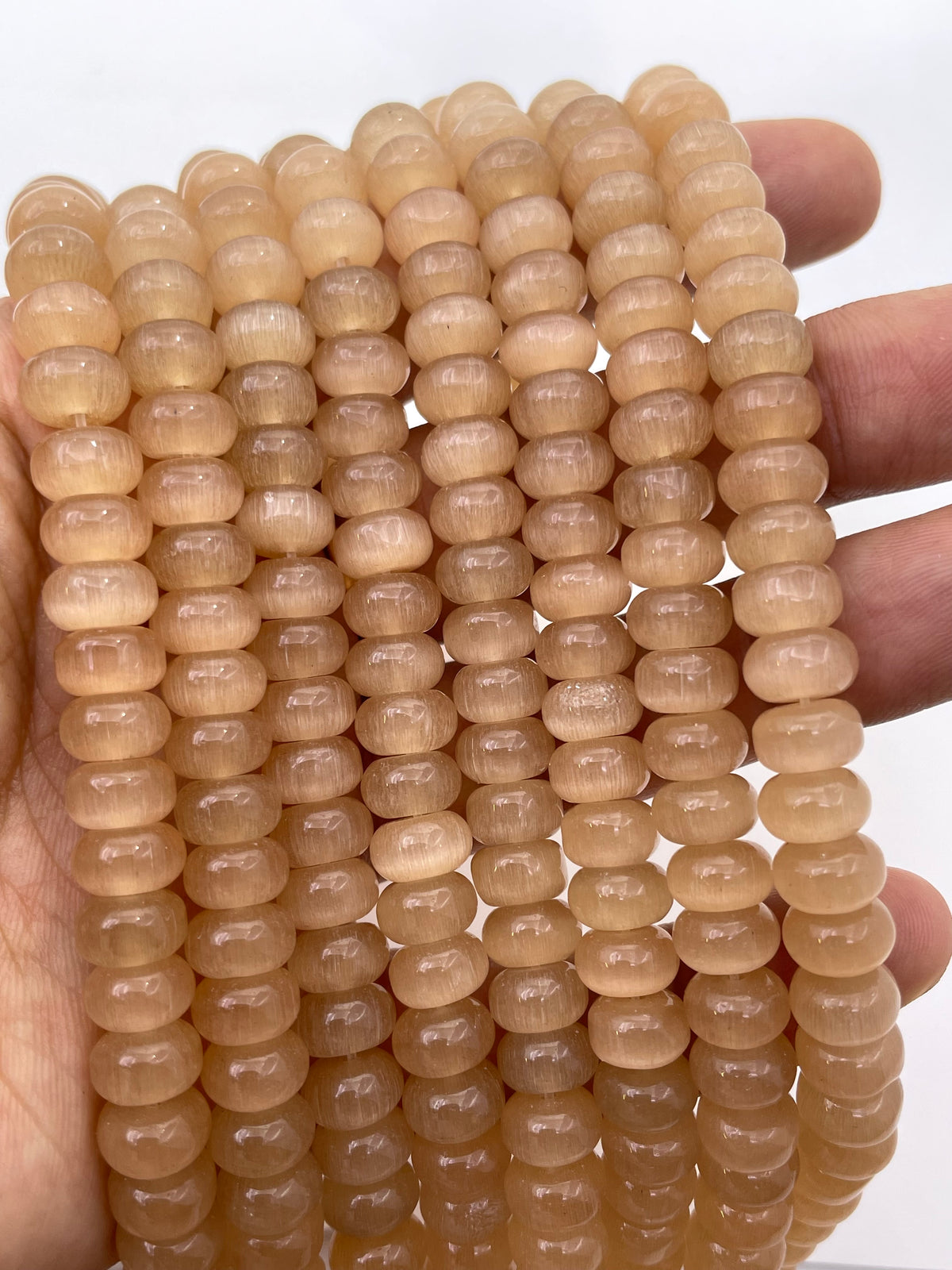 A close-up of multiple strands of smooth, round, translucent cats eye beads held in a person's hand against a plain white background.