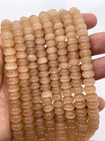 A close-up of multiple strands of smooth, round, translucent cats eye beads held in a person's hand against a plain white background.