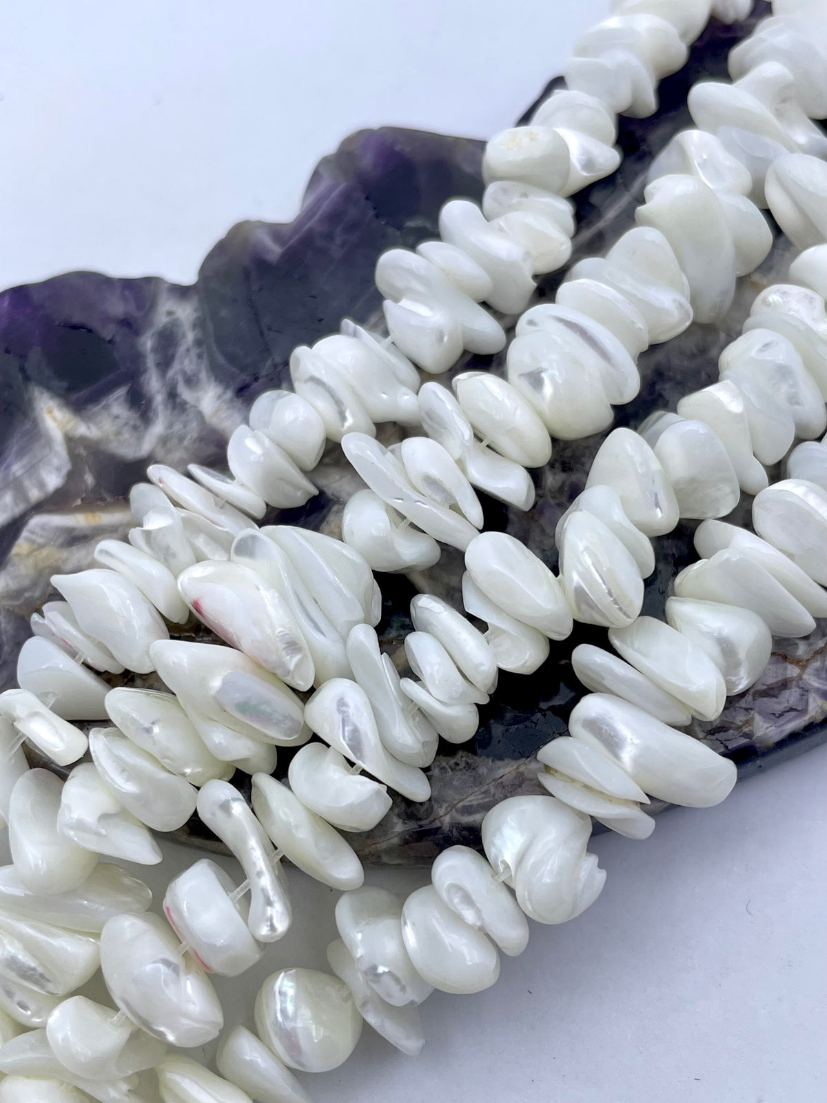 White irregular shell beads or pearls arranged on a dark amethyst crystal slice against a plain white background.