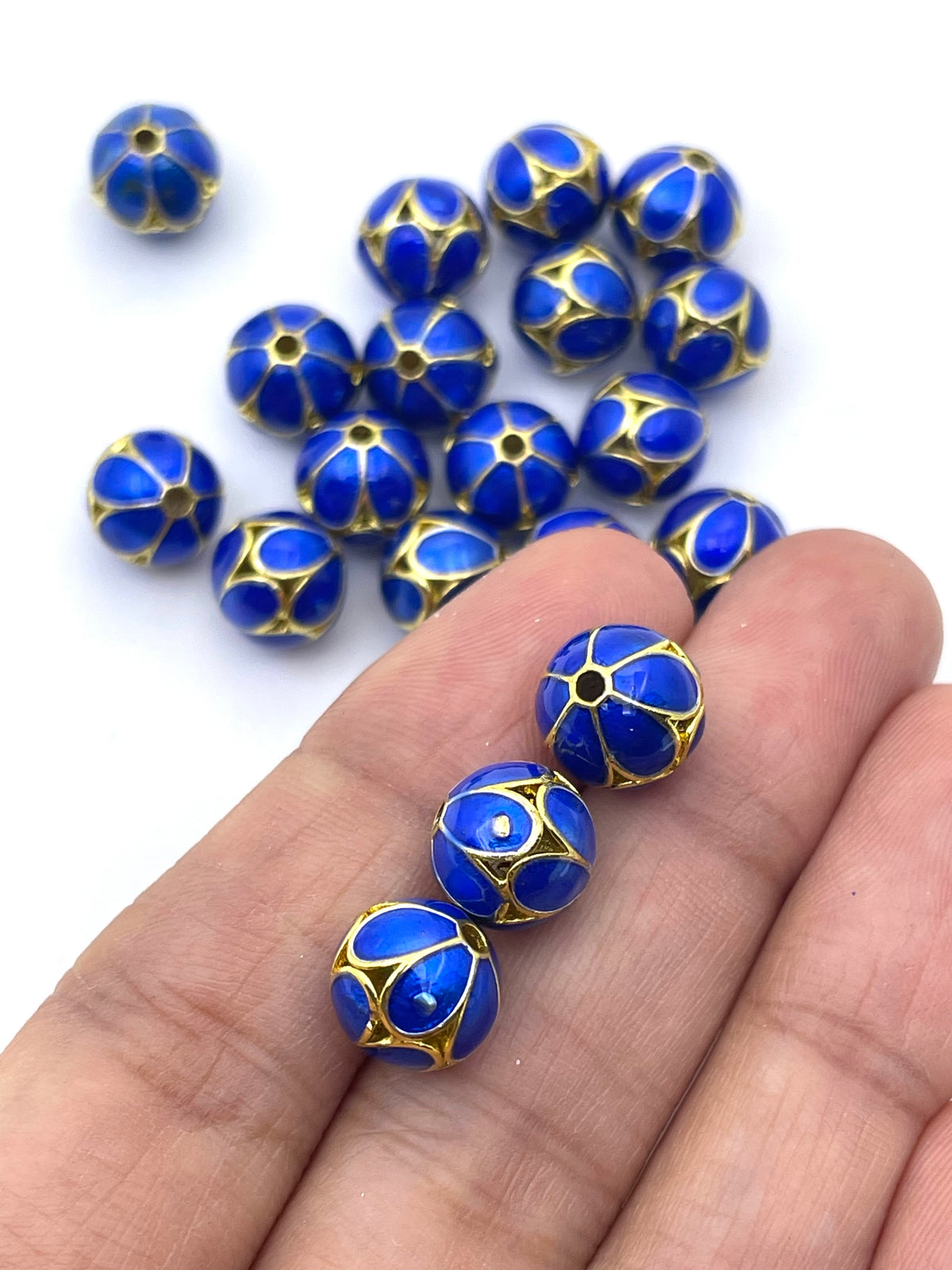 Blue and gold decorative beads with a starburst pattern, shown resting on a person's hand with additional beads scattered in the background.
