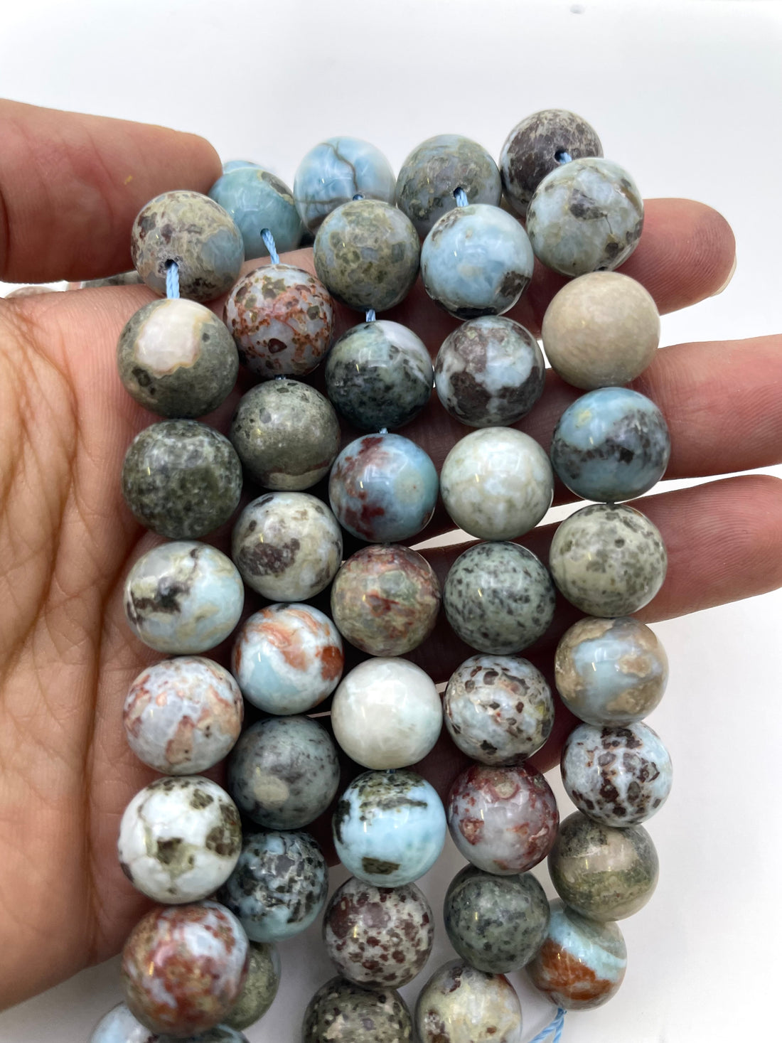 Round polished larimar gemstone beads in a marbled pattern of light blue, green, beige, brown, and white, arranged on a plain white background.