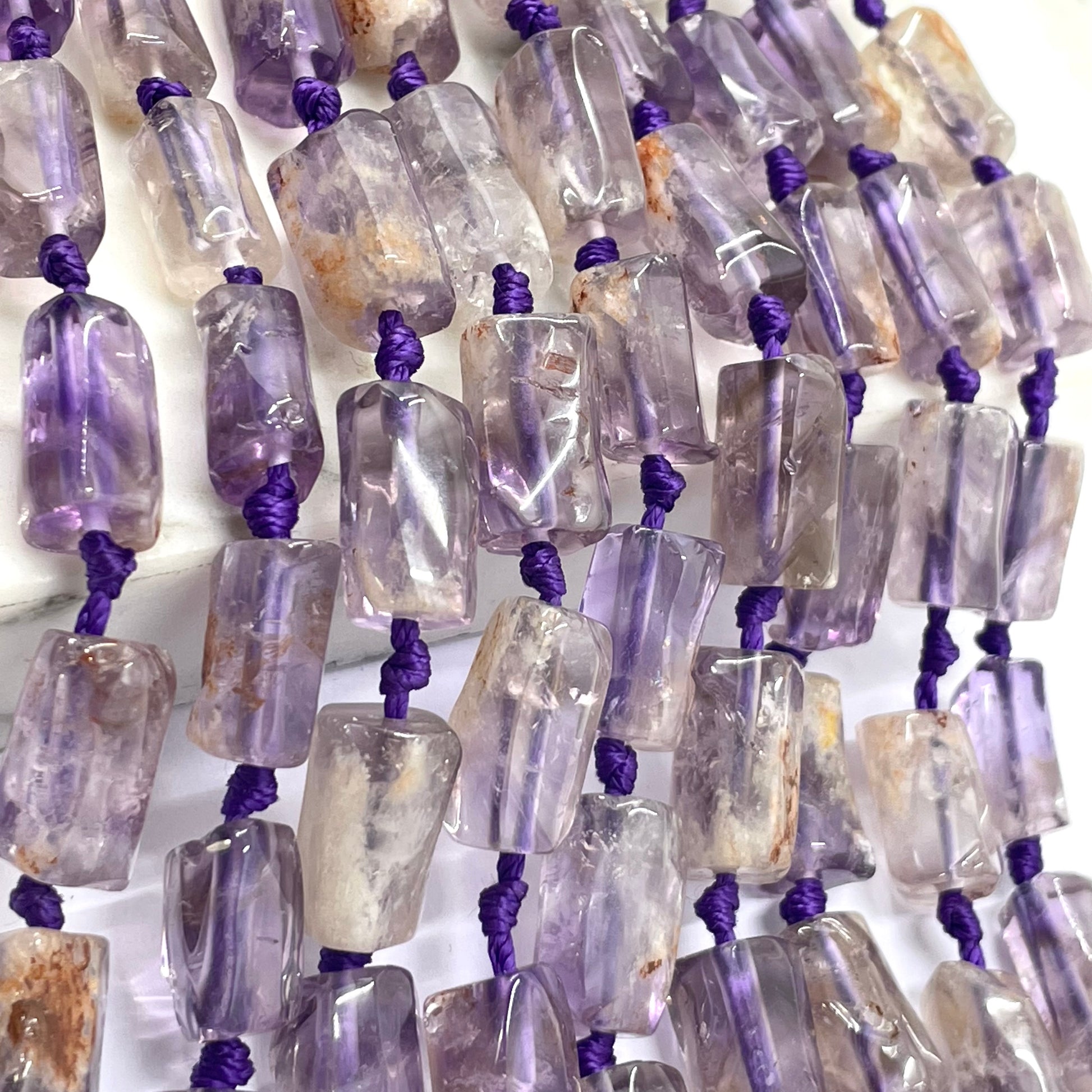 Purple phantom rectangular beads threaded on a purple cord, shown in a close-up view against a white background.