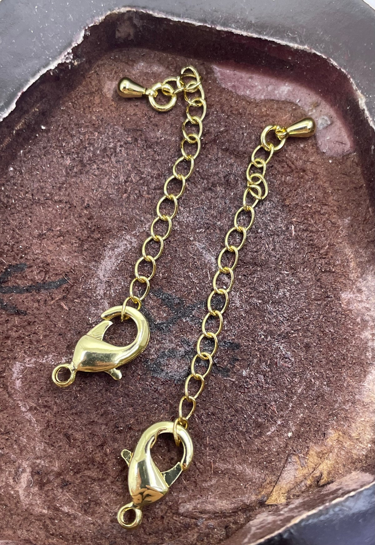 Two gold lobster claw clasp chain extender straps with spring rings, displayed on a textured brown stone surface.