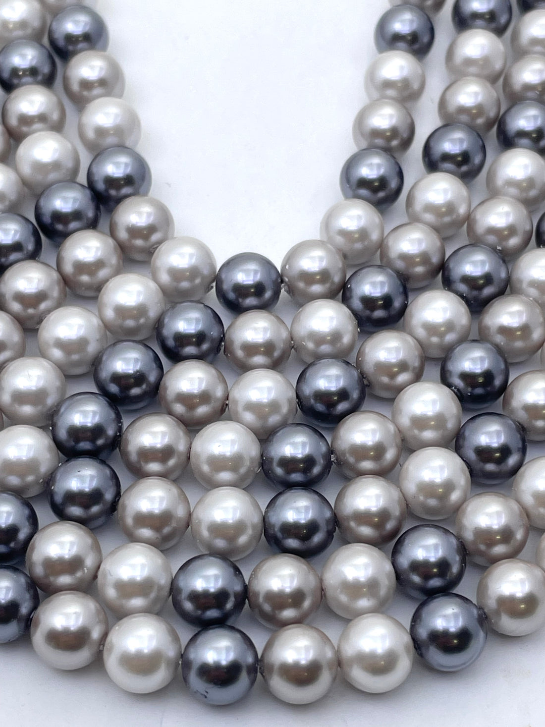 A close-up of shell pearl beads in mixed colors, including cream, light gray, charcoal, and dark navy, arranged in overlapping rows.