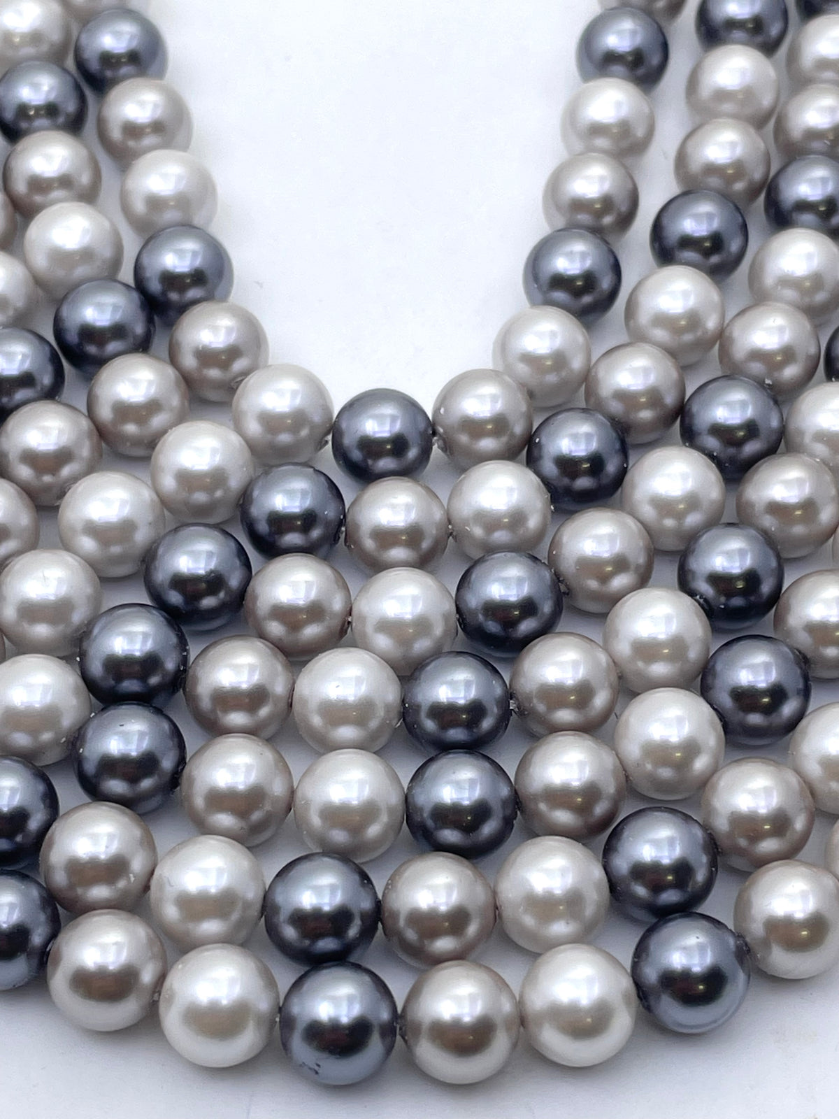 Multiple strands of shell pearl beads in mixed colors including white, gray, and dark charcoal, arranged in a layered V-shape on a light background.