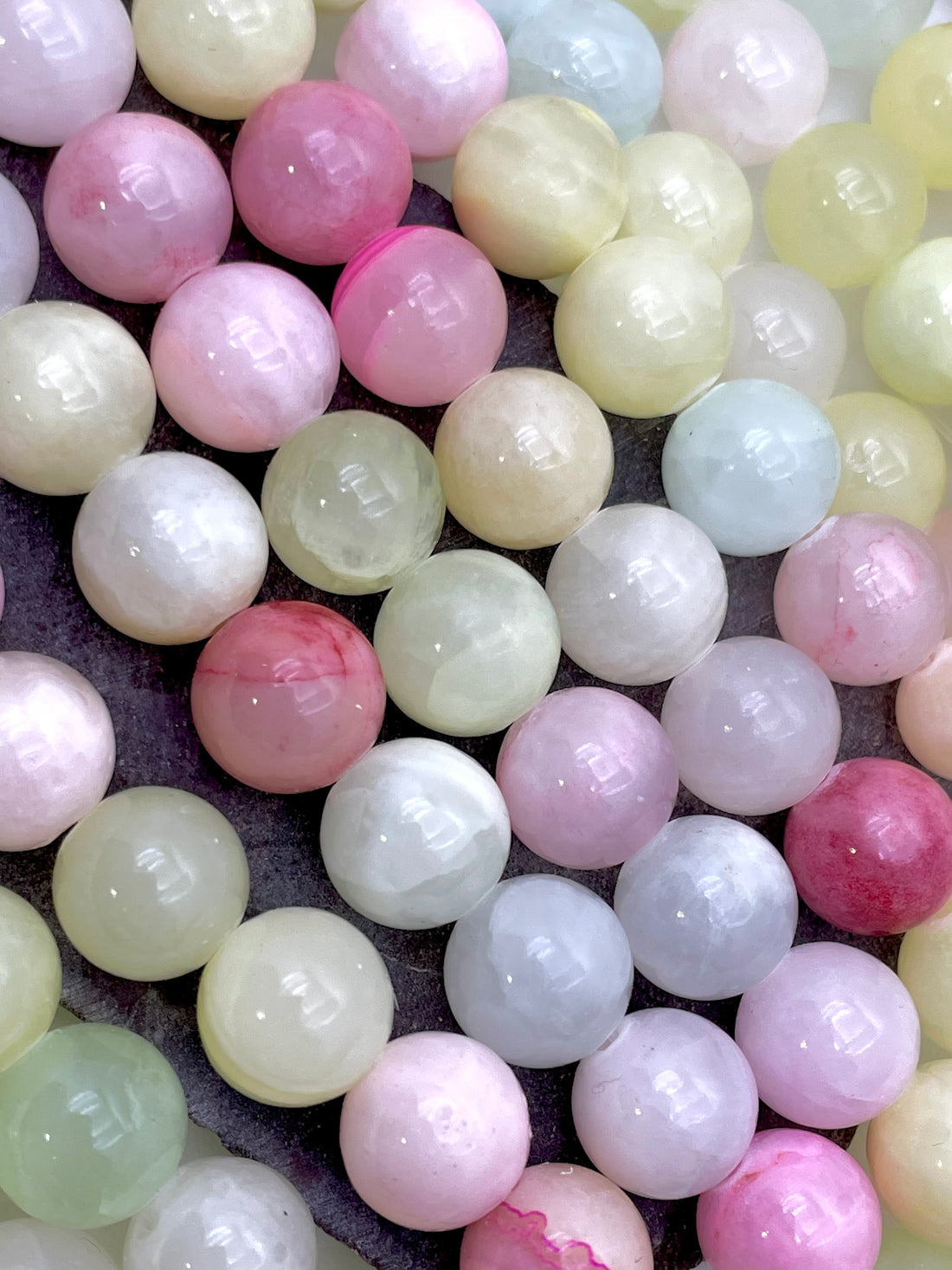 A close-up of a hand holding a strand of polished round jade gemstone beads in pastel colors, including pink, green, yellow, blue, and white.