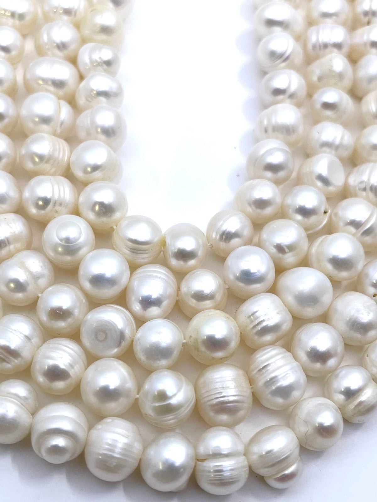 Close-up of multiple strands of white freshwater pearl beads threaded on a black cord, arranged in a U-shape against a plain white background.