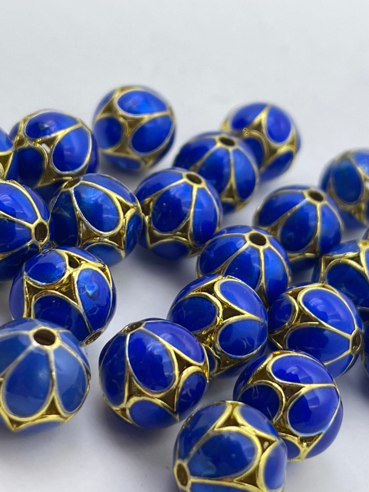A pile of round blue beads with gold geometric filigree patterns on a light gray background.