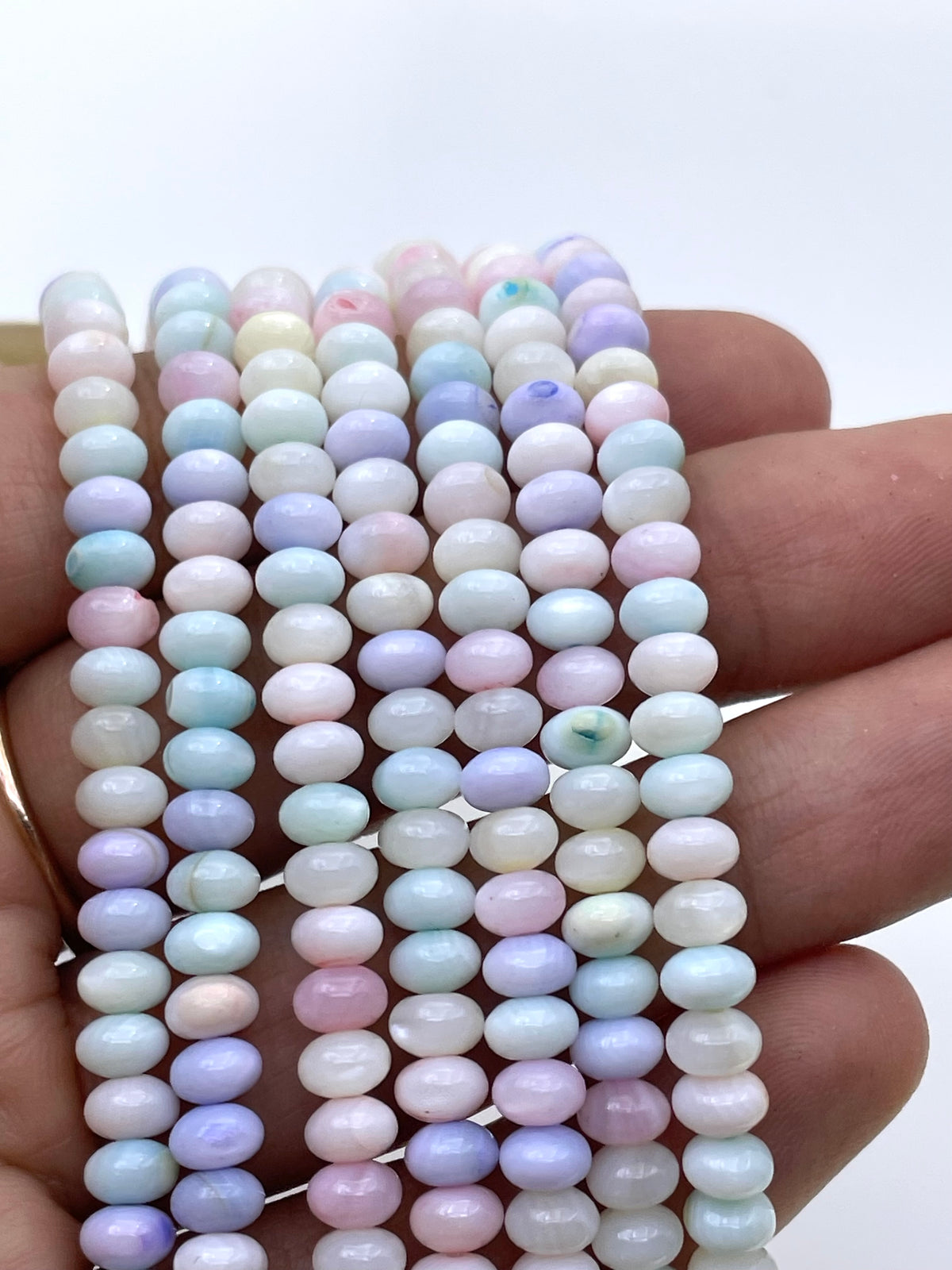 Multiple strands of small oval beads in pastel shades of pink, blue, purple, green, and white, held in a person's hand against a plain light background.