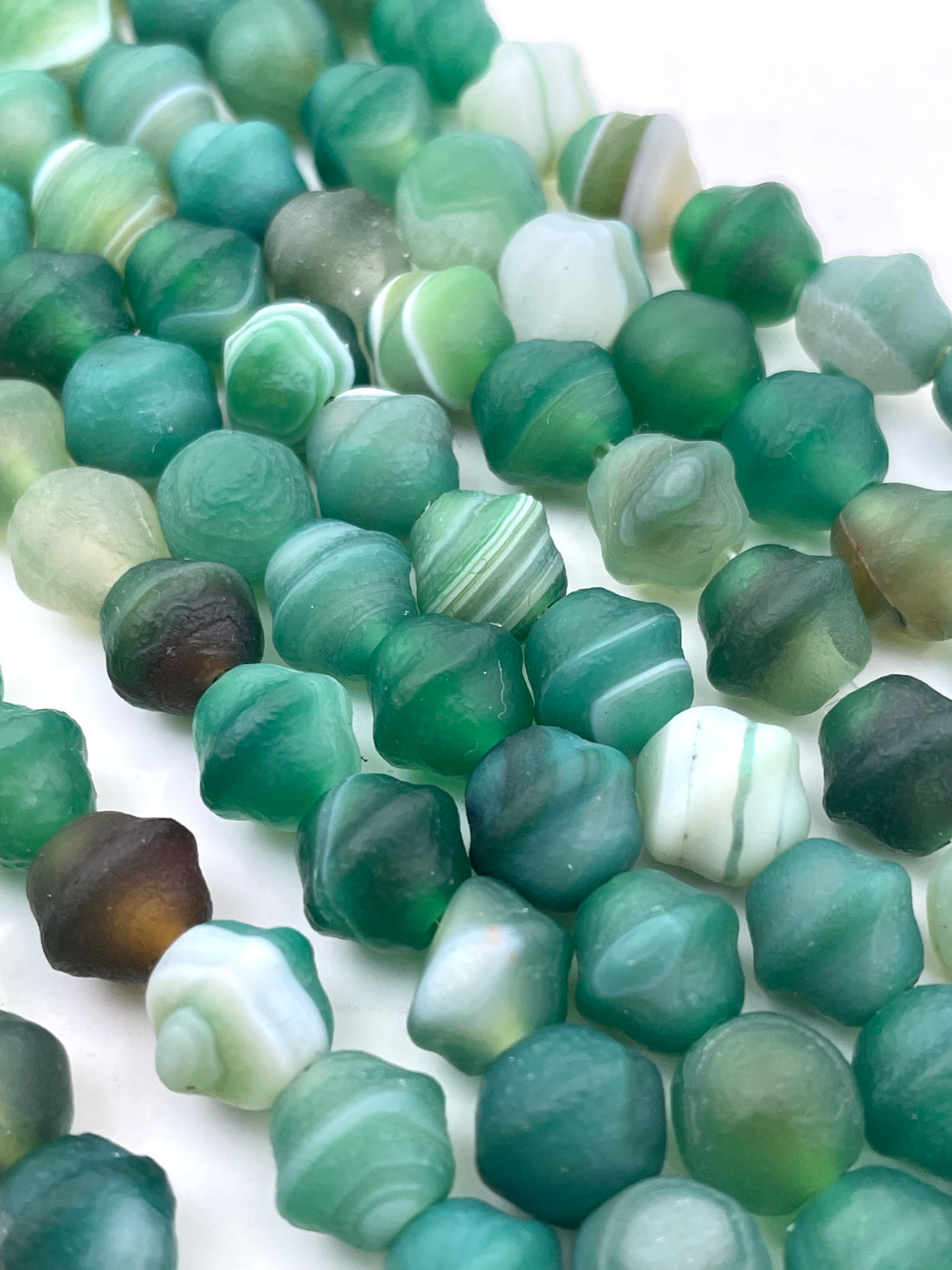 Close-up of multiple green banded agate beads with some white banded sections, arranged on a plain white background.