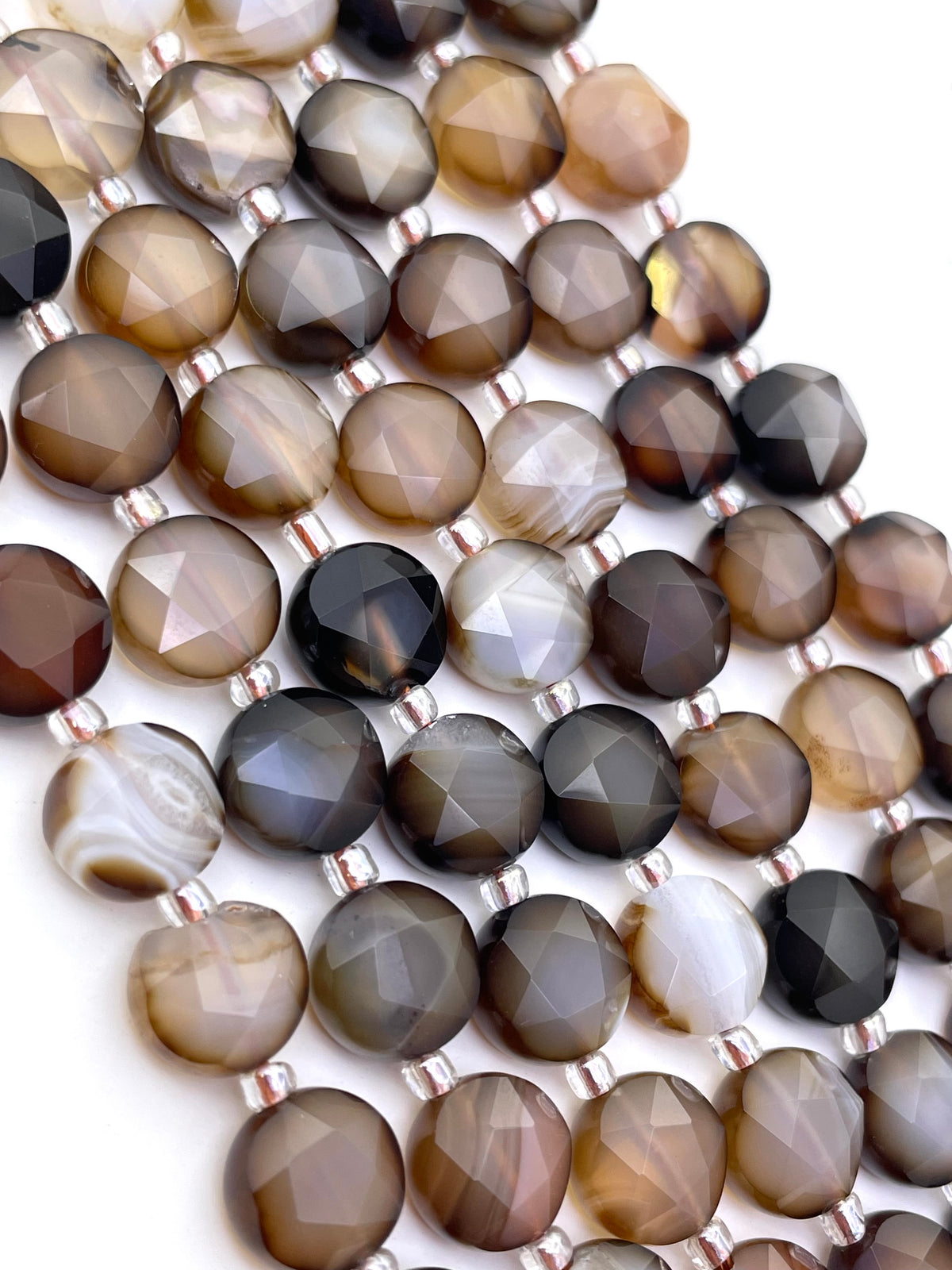 Faceted round botswana agate beads in shades of brown, gray, black, and white, strung on silver wire against a white background.
