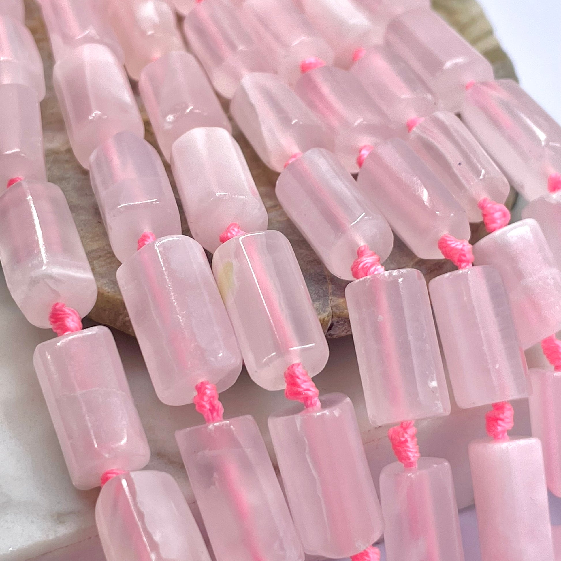 Pink translucent rectangular calcite  beads strung on a cord with bright pink thread, photographed close up on a light stone surface.