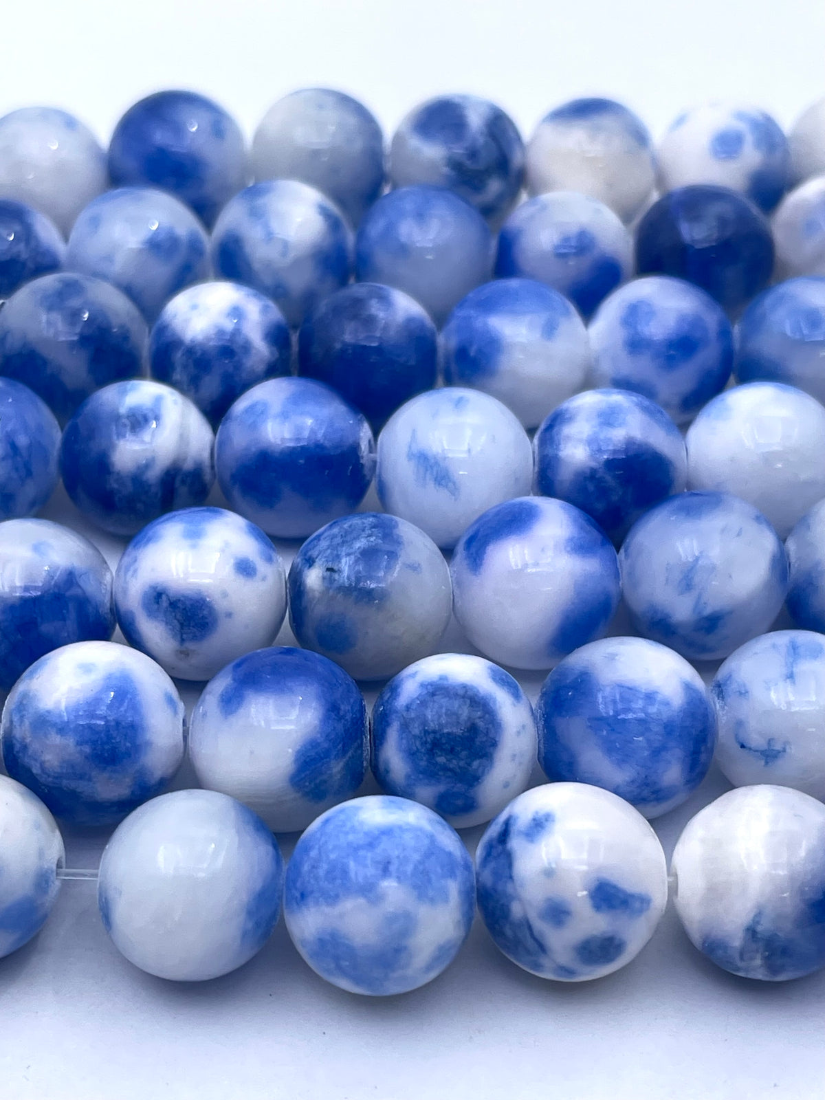 Blue and white marbled round persian jade beads arranged in rows on a plain white background.