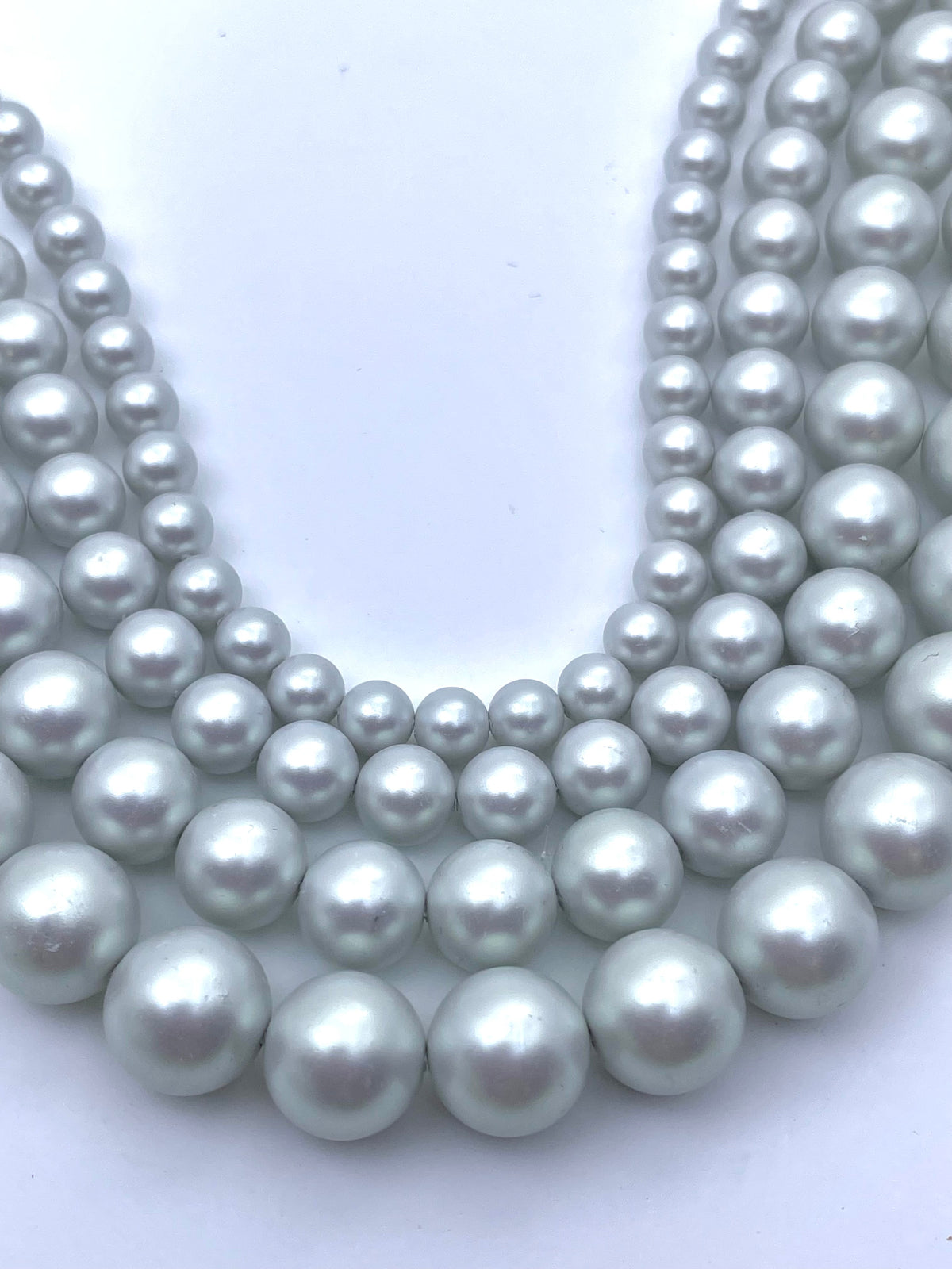 Multiple strands of grey silver shell pearl beads arranged in concentric rows on a plain white background.