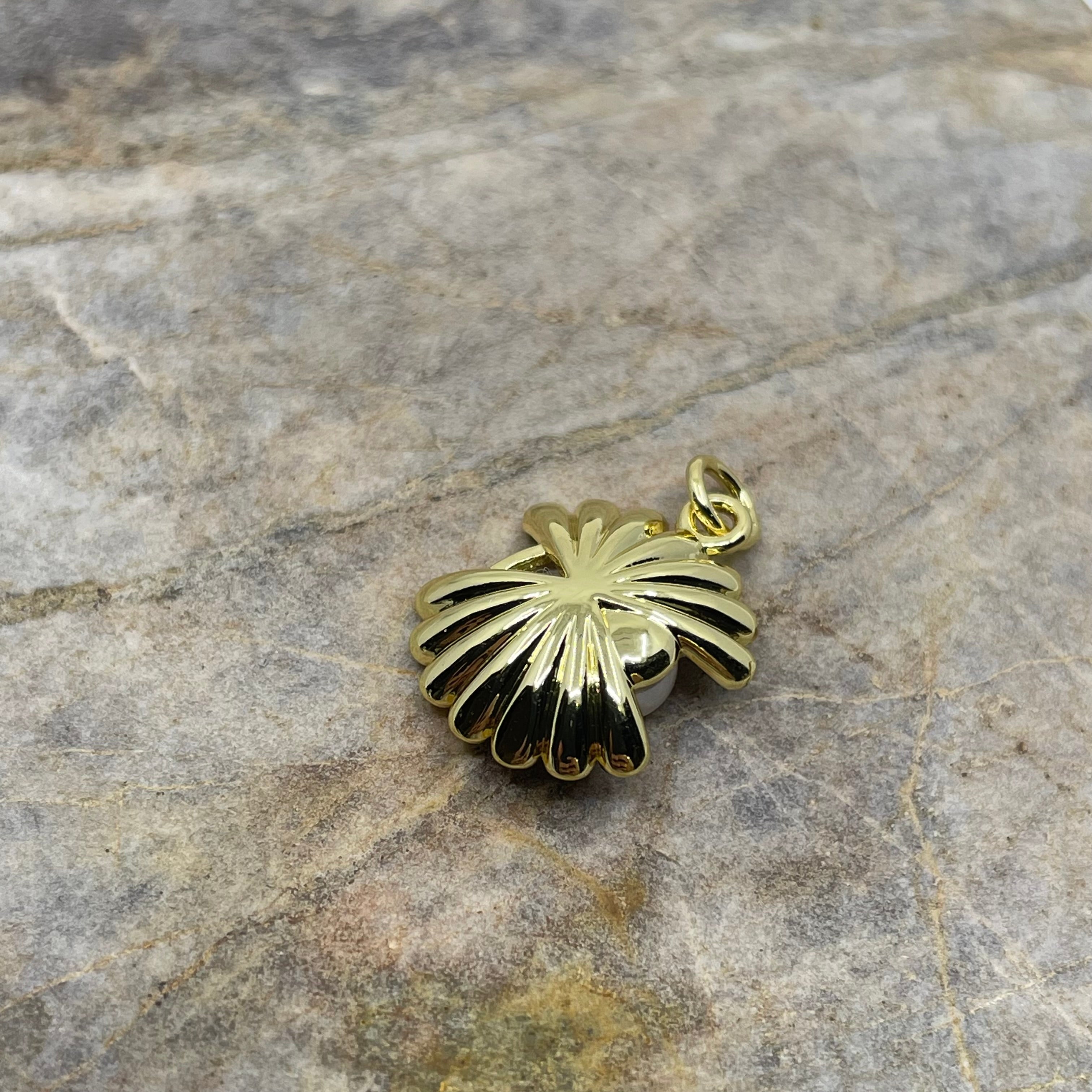 A gold-toned shell-shaped pendant with black enamel inlay, resting on a textured gray stone surface.