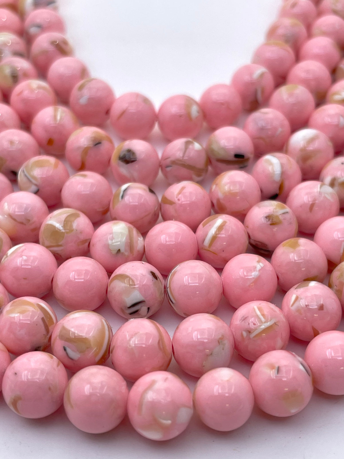 Pink round mop beads with white, black, and gold marbled swirls, arranged in strands on a white background.