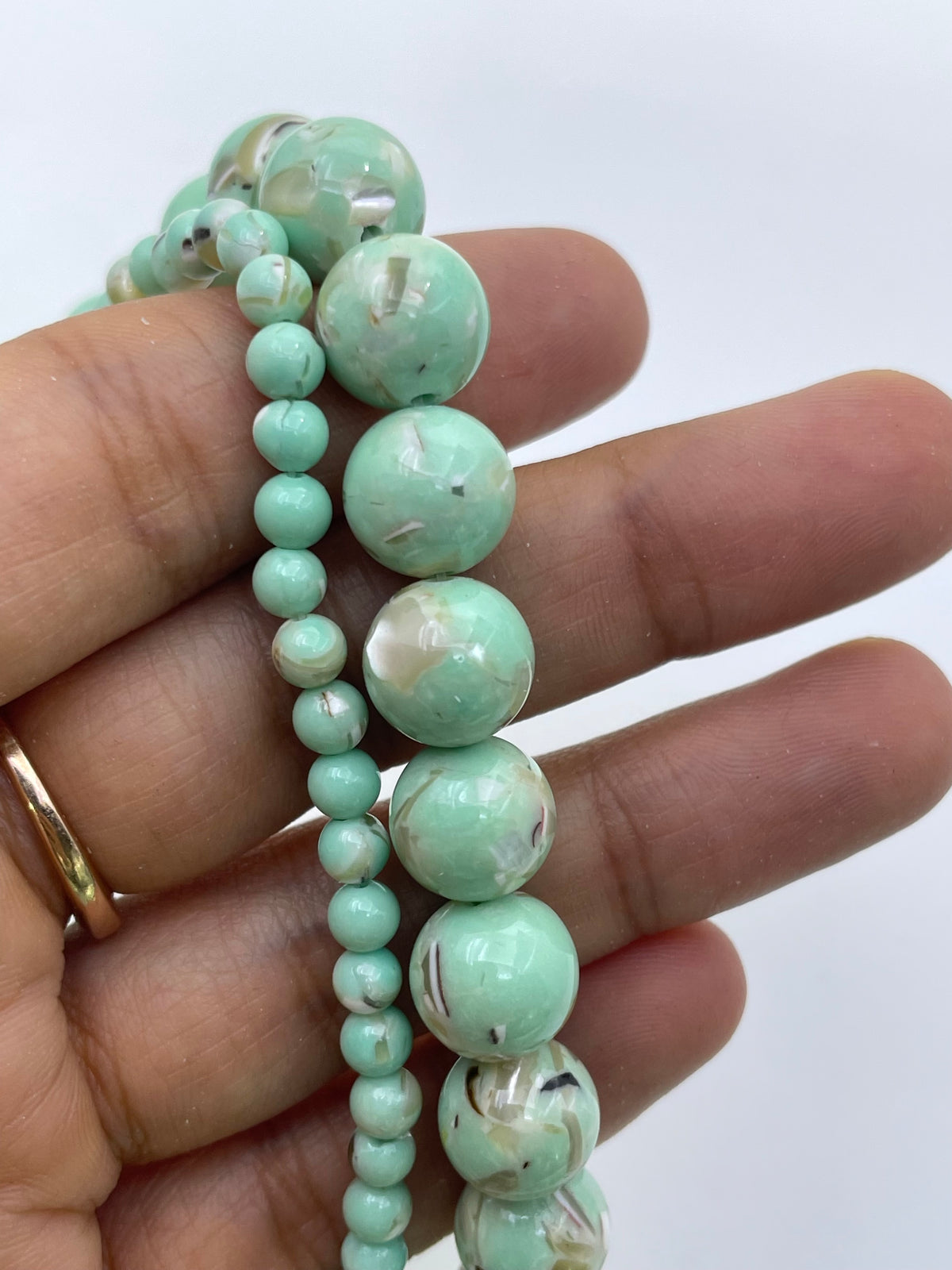A close-up of a hand holding two strands of light green marbled mop beads.