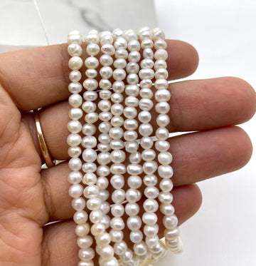 A hand holding several strands of white freshwater pearls, with a gold ring visible on the ring finger, against a light background.
