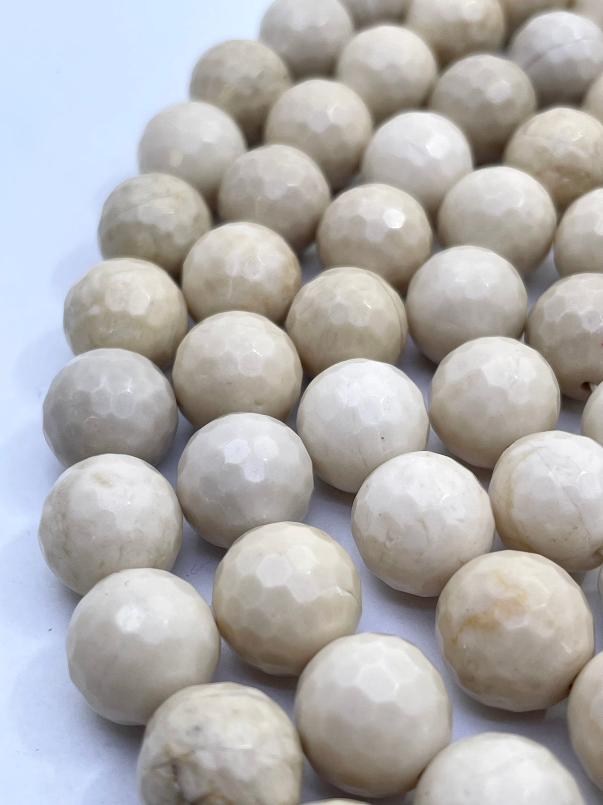 Faceted round fossil stone beads in a warm cream or ivory tone, arranged in diagonal rows on a plain light background.