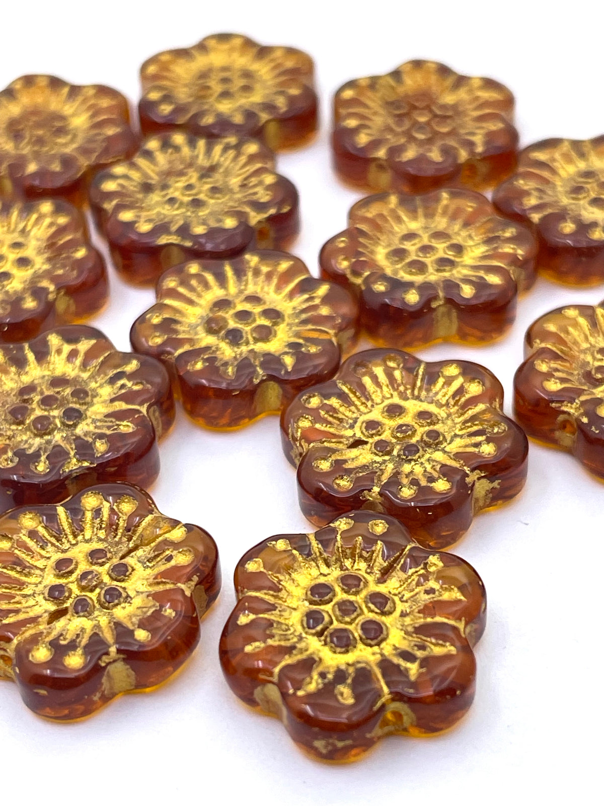A cluster of small, flower-shaped translucent amber beads with a raised gold floral pattern, arranged on a plain white background.