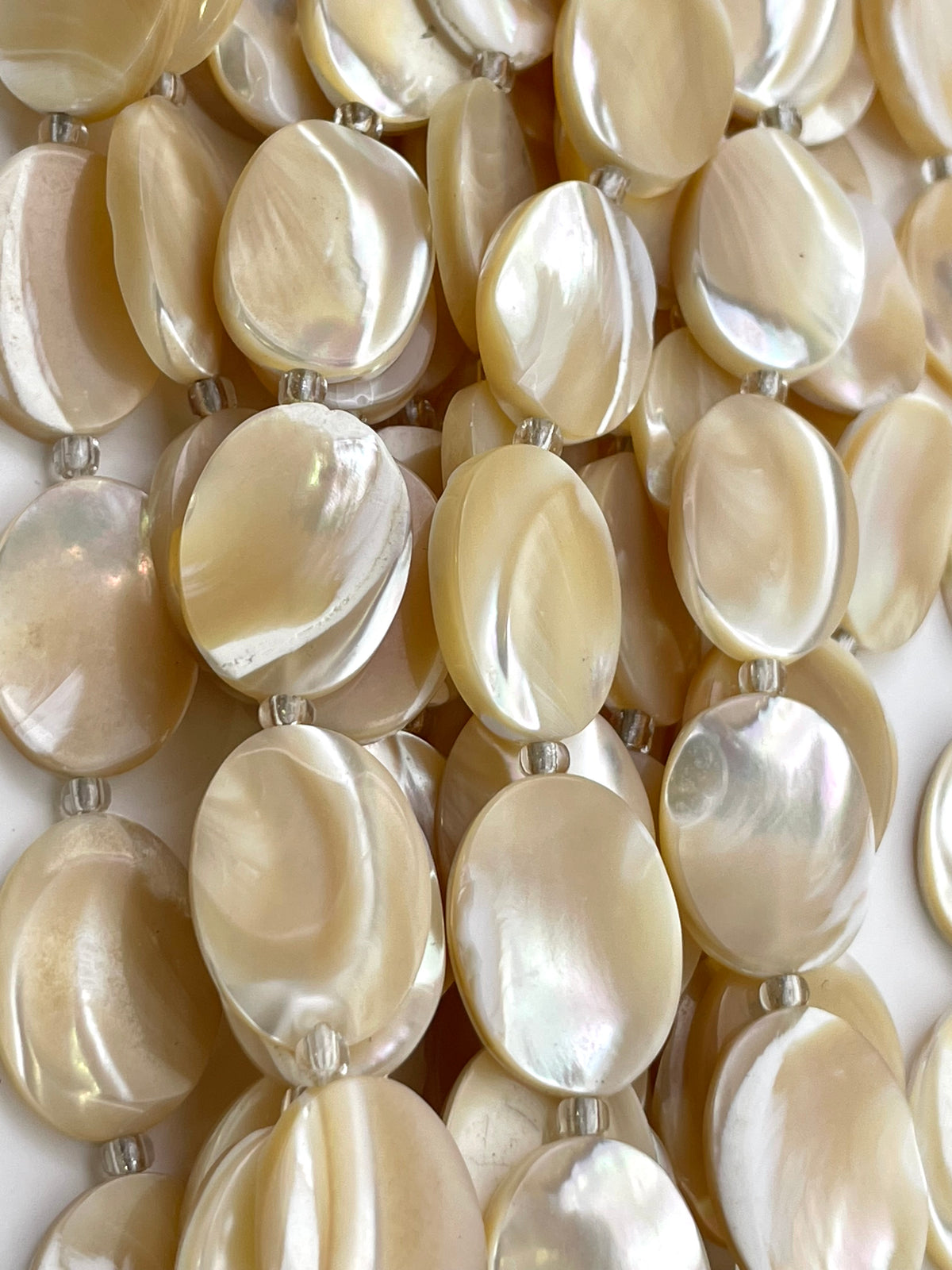 Close-up of a strand of oval mother-of-pearl beads with a glossy, iridescent finish, strung on silver beads.