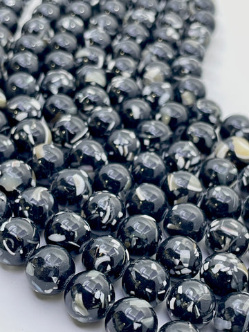Close-up of glossy round mop beads in a black and white marbled pattern, arranged on a white surface.