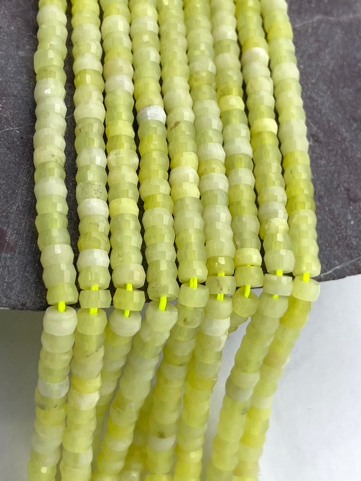 Faceted lemon jade beads in pale yellow-green and cream tones, strung in multiple strands on a dark gray surface.