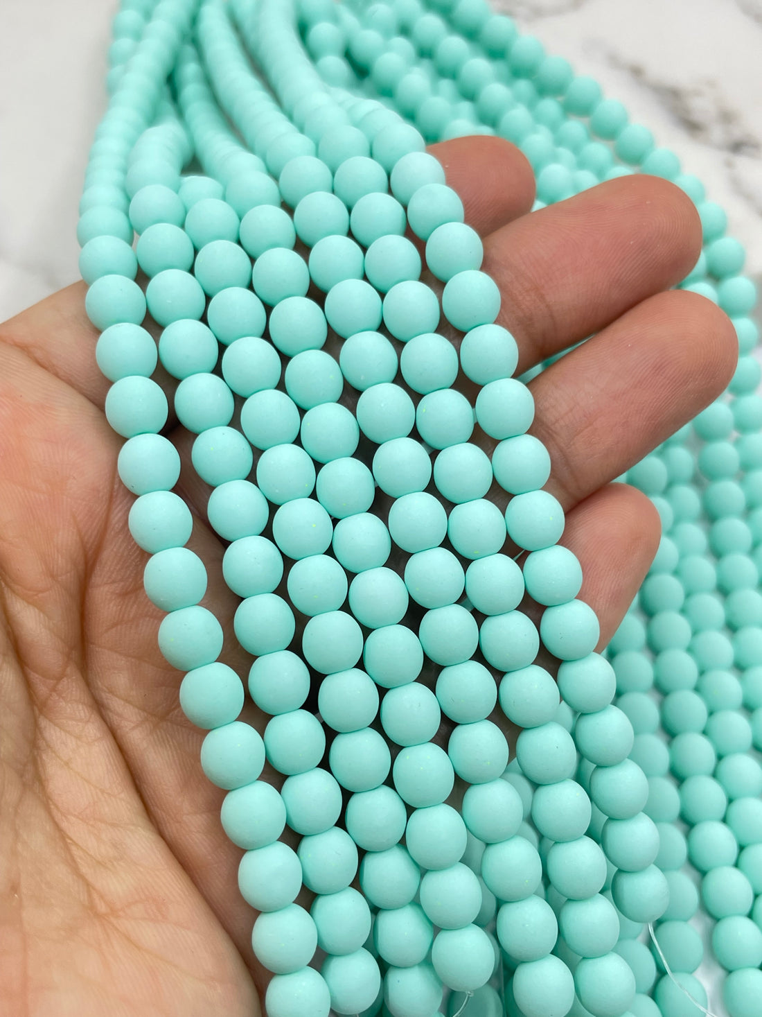 A close-up of seafoam blue velvet beads arranged in rows, with a marble-like surface visible in the background.