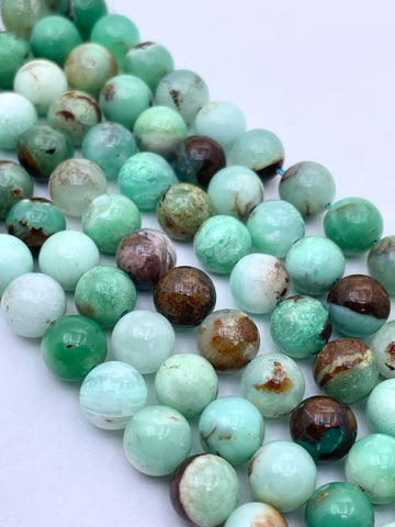 Round natural chrysoprase stone beads in shades of mint green, light aqua, white, and brown, arranged in a curved line on a plain white background.