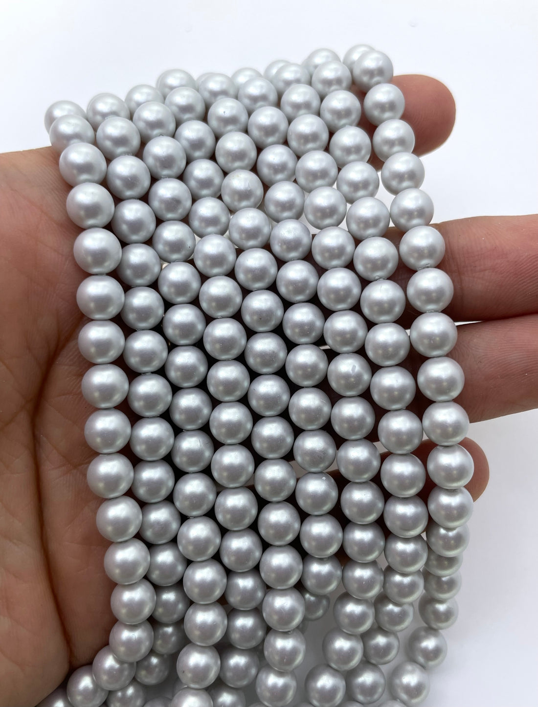 Multiple strands of round, iridescent shell pearl beads in a light silver-gray color, arranged in a V-shape on a plain white background.
