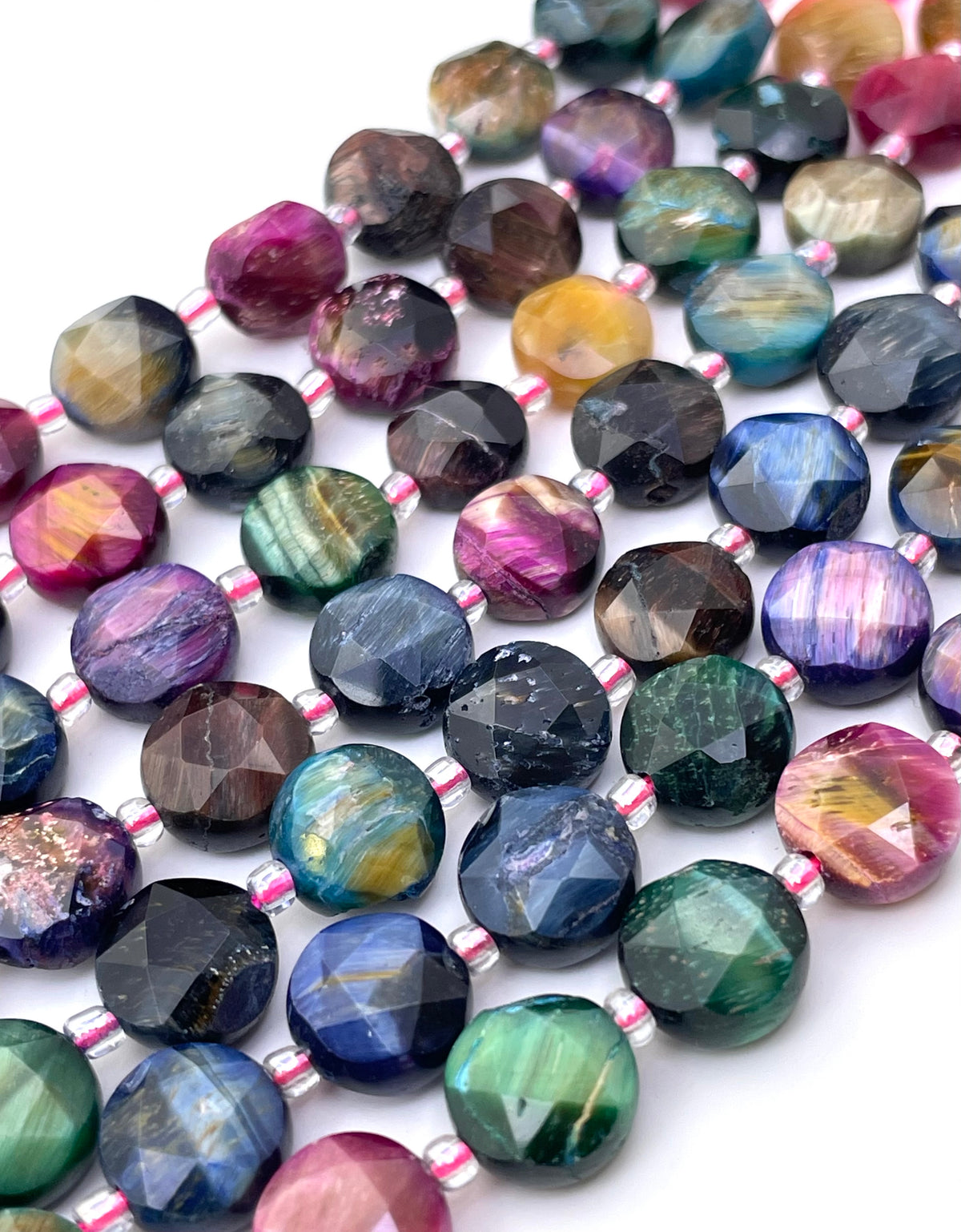 Faceted round galaxy tiger eye gemstone beads strung on a pink and white cord, arranged in diagonal rows on a white background. The beads display a wide variety of colors and patterns, including blue, green, purple, pink, yellow, and brown.
